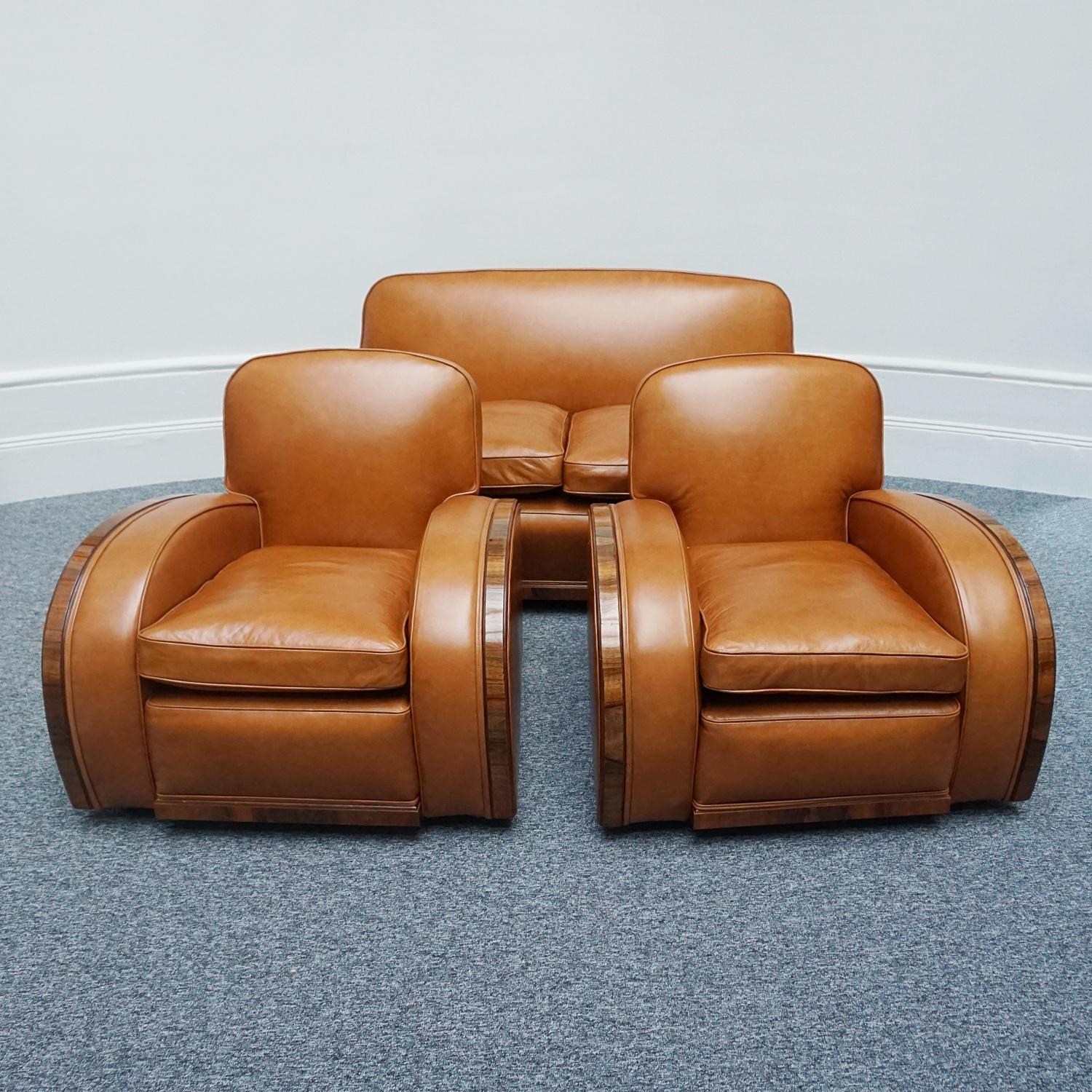 An Art Deco three piece tank suite by Heal's of London. Comprising a tank sofa and two tank chairs. Figured walnut banding throughout with light brown leather re-upholstery. Set over vintage castors. 

Dimensions: Sofa H 76cm W 164cm D 81cm Chairs