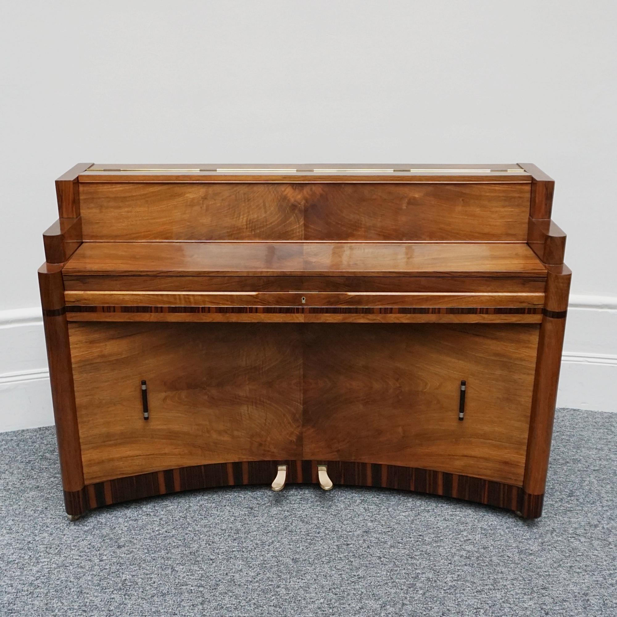 An Art Deco Steck Mini Piano. Burr and figured walnut throughout with macassar ebony banding. Original bakelite and metal handles to lower section. Original retailers mark to right hand side. Matching stool included but not photohraphed as currently