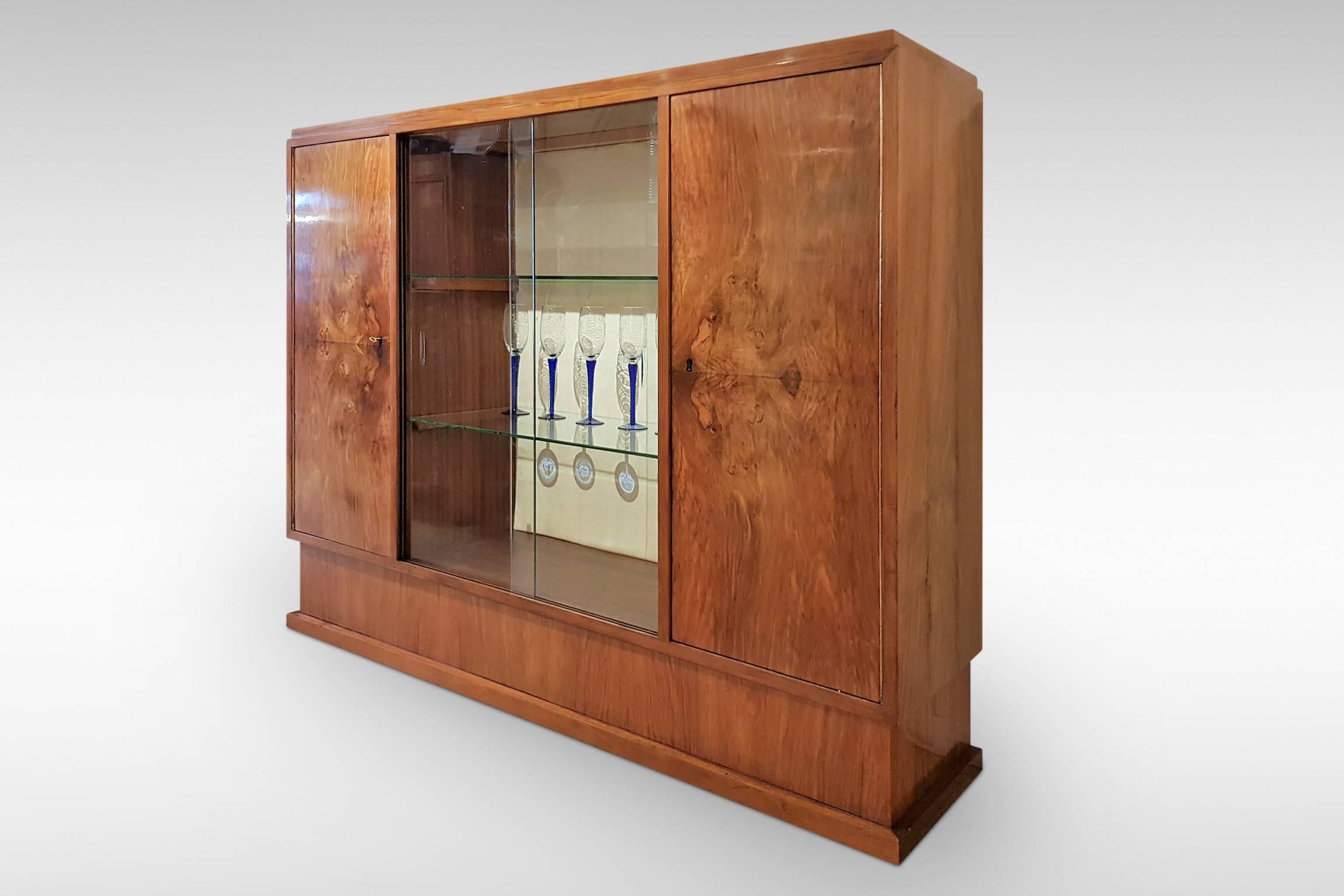 A handsome and fine quality modernist display cabinet from the Art Deco period. It has stunning figured Walnut veneers and features piano hinges to the flanking cupboard doors.