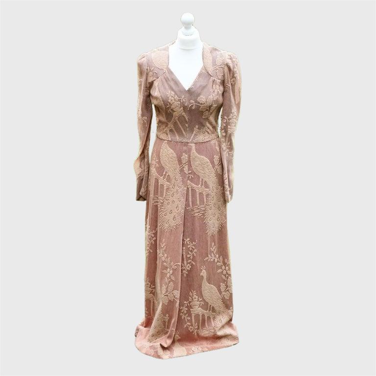 
Magnifique robe longue en maille beige rosé de Biba, ornée d'un magnifique motif de paons et de fleurs, avec un col en V. La robe est doublée de satin gris et rose au niveau du corsage et de la jupe. La doublure pourrait avoir été ajoutée