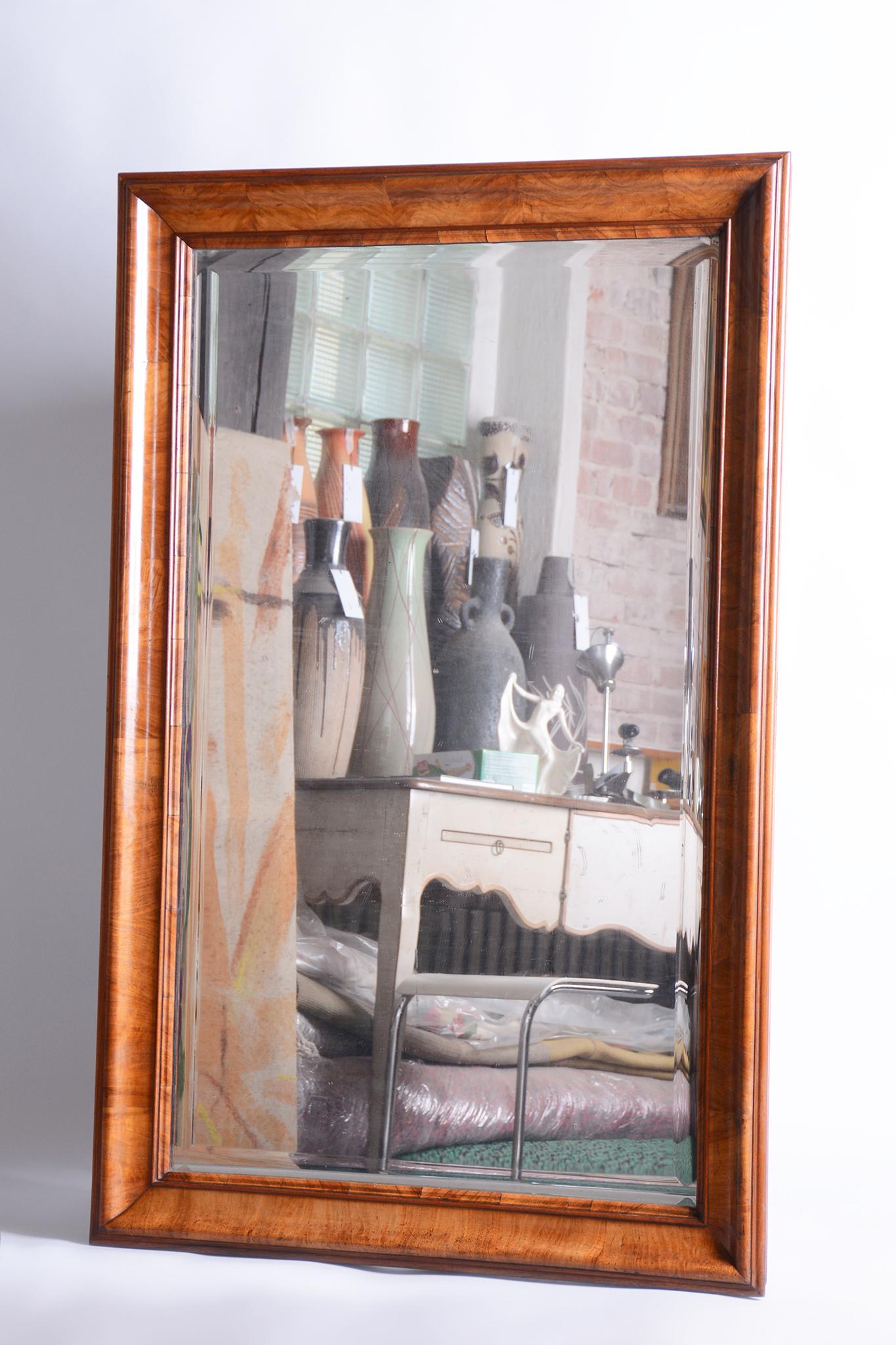 Cet élégant miroir mural de style Biedermeier provient de Bohemia et date de la première moitié du 19e siècle. Le cadre du miroir est plaqué de noyer et le miroir lui-même est biseauté. Il a été conservé dans un très bon état d'origine et son poli a