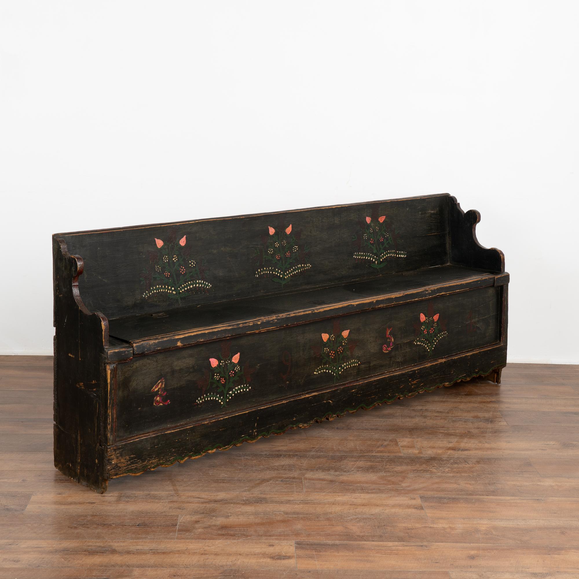 Original hand painted black folk art pine bench with simple floral/vine folk art embellishments along the front and back; dated 1951. 
Unique to this bench is the narrow depth at only 13