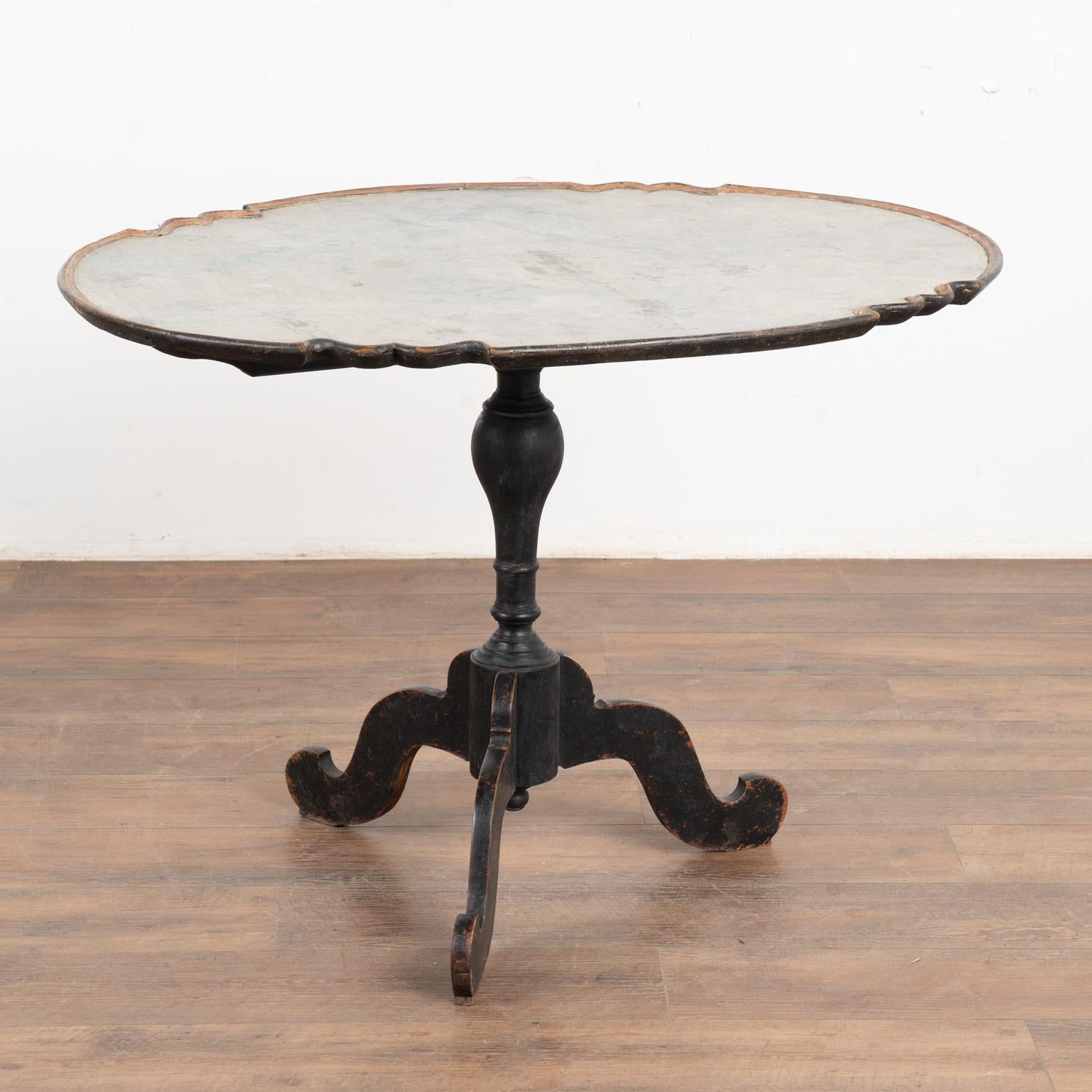 The aged patina of the original black paint accentuates the curves and grace of this Rococo tilt top side table. Note the top was hand painted with a traditional faux marble finish in varied layers of light blue, white and gray.
The black painted