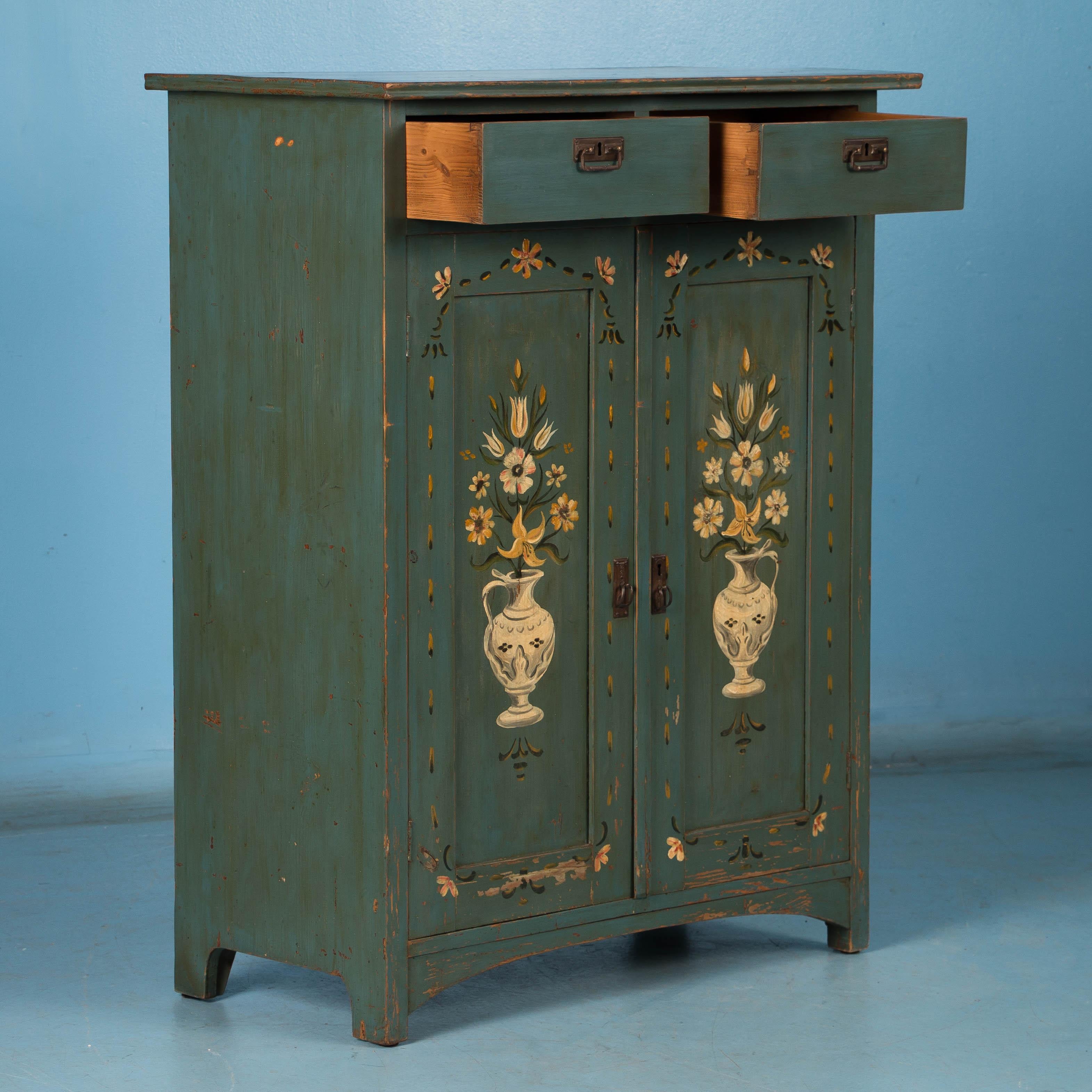 While you can frequently still find antique pine cabinets, it is difficult to find one with exceptional original paint such as this one. The two panel doors are painted with a traditional flower basket motif against a lovely blue / green black