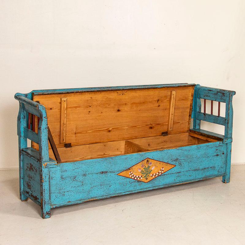 Bright and cheerful, this 6' bench has hidden storage under the hinged seat which was a traditional element in this style of bench throughout the 1800's in Europe. The festive blue paint is all original, and accented by a colorful flower motif with