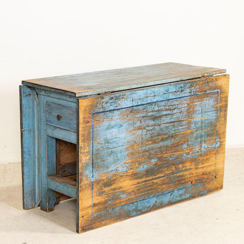 There is wonderful charisma to this sweet drop leaf table due to the varied colors of blue paint layered on through the years and now softly distressed. Unique to this table is the single, extremely long drawer that extends almost the entire width