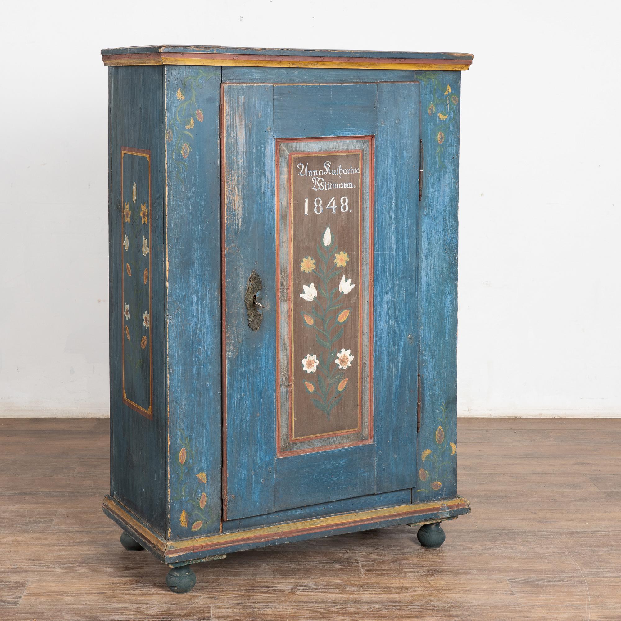 This charming single door pine cabinet still maintains its original blue painted finish with red and yellow trim, with date of 1848 and flowers embellishing the front and sides.
Distress to the painted finish reflects generations of use, and is worn