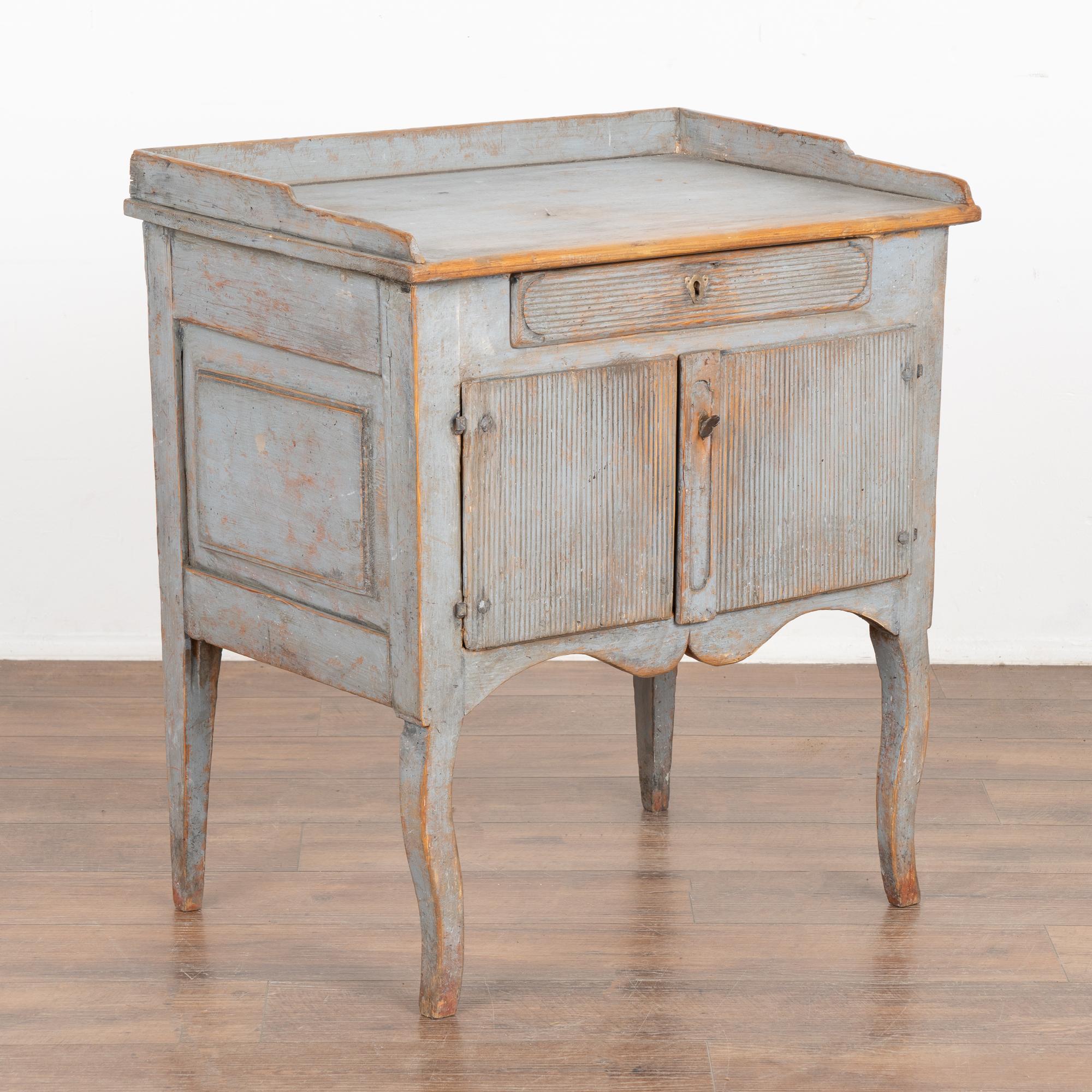 Small Swedish country cabinet standing on tapered/curved legs that may serve also as a nightstand or side table. The original blue painted finish has been distressed through generations of use, adding to its authentic vintage appeal.
A single drawer