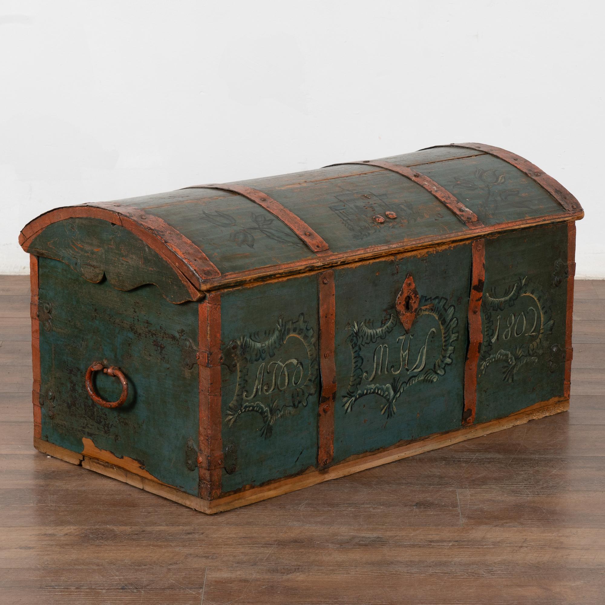 Original painted dome top oak trunk from Sweden with traditional hand-painted details include floral and central house motif along top front.
The original blue painted finish has undertones of teal and is accented by the muted red painted straps and