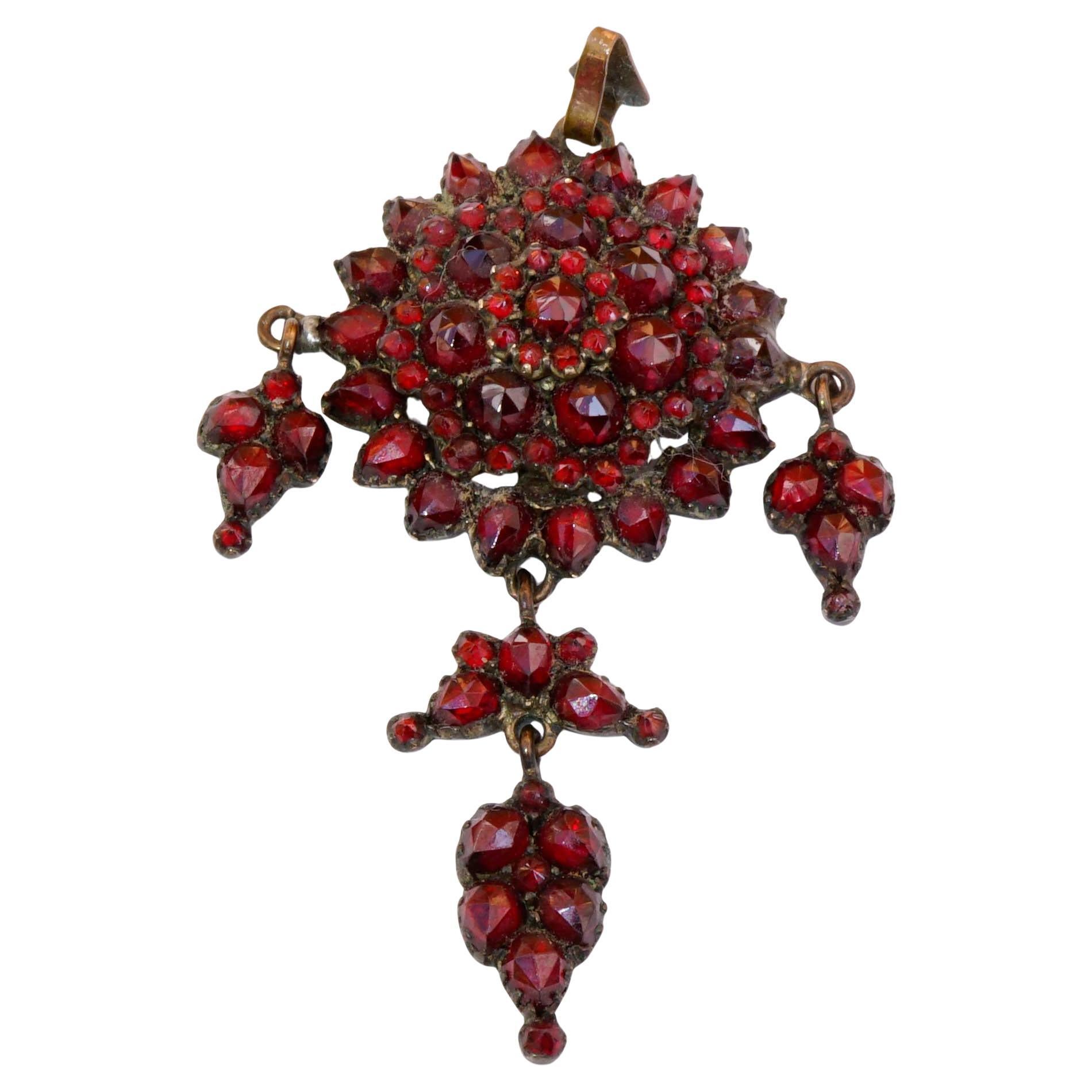 This fine pendant was made in Bohemia circa 1860-1890. The star design consists of 5 rows with numerous rose cut  faceted garnets and three small and bigger pendants. The pendant is set in a material called tombak with original carbuncle stones in a