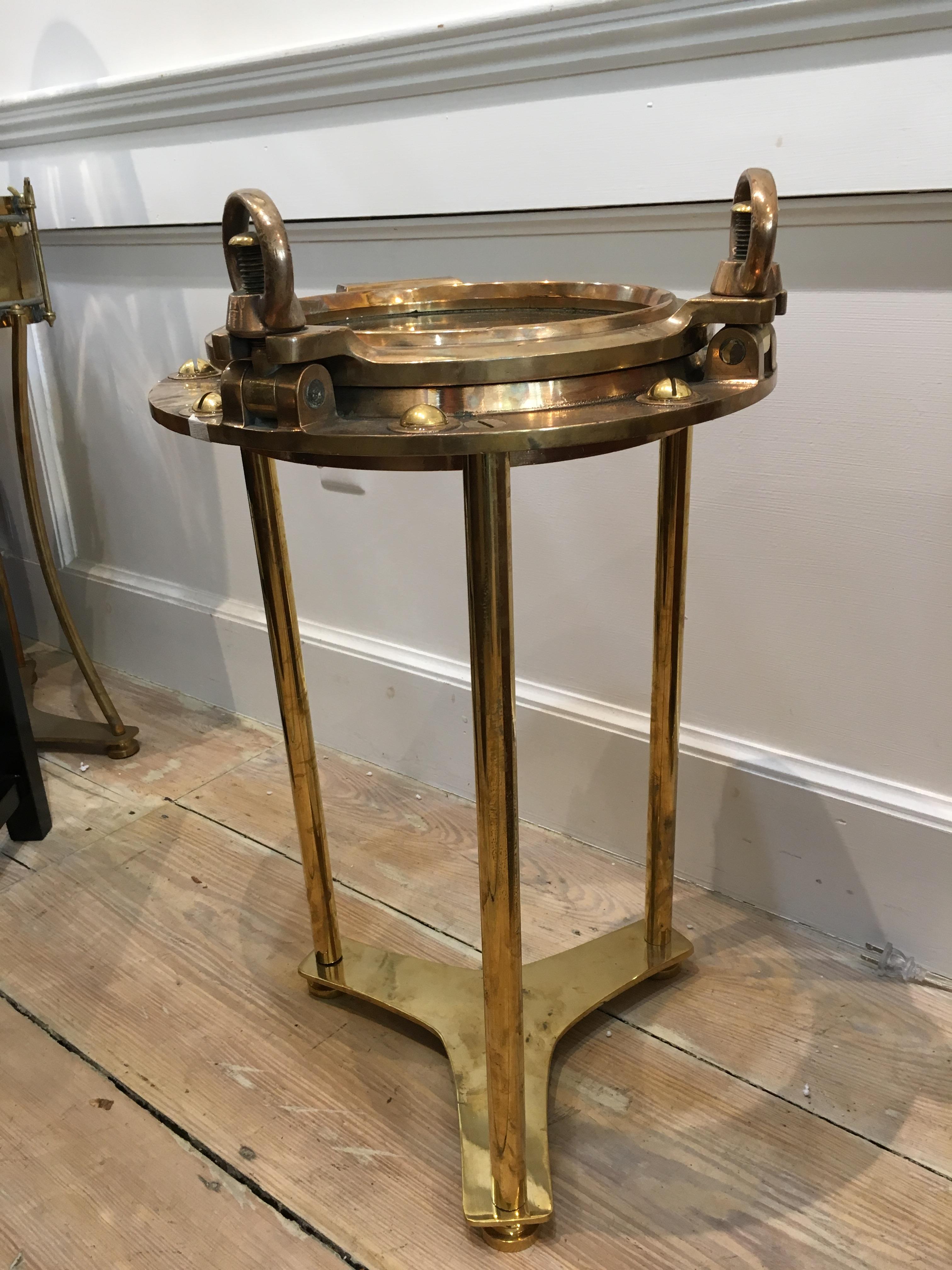 An original brass ship's porthole window complete with working double keys that still open the window. The rivets have been replaced as these pop out when taken off the ships. Polished, but still has original patina. The table base has been designed