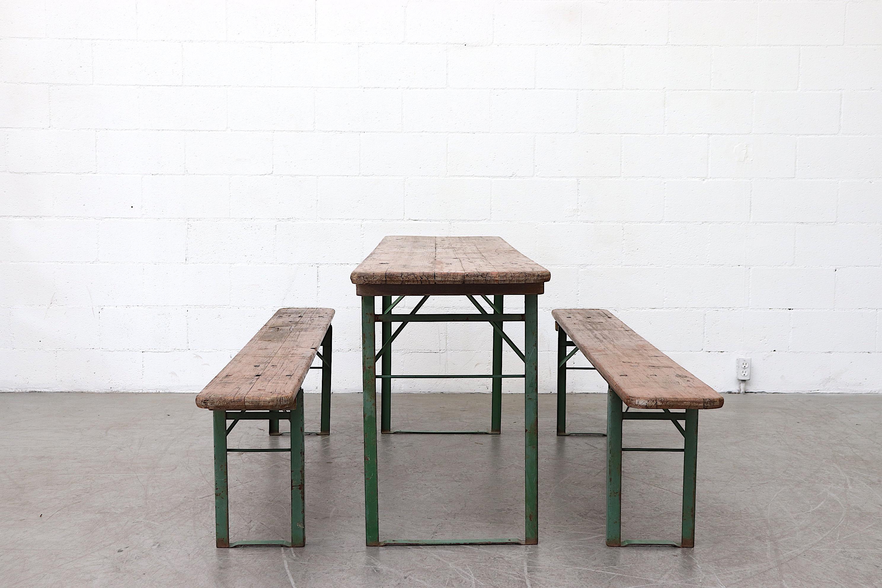 Wood topped folding tables and benches, sold as a set of 2 benches and 1 table. Metal is in original condition with visible patina. Wood in original used condition as well. Sets vary in color and wear. Benches measure 86.5 x 10.5 x 18.5. Set price.