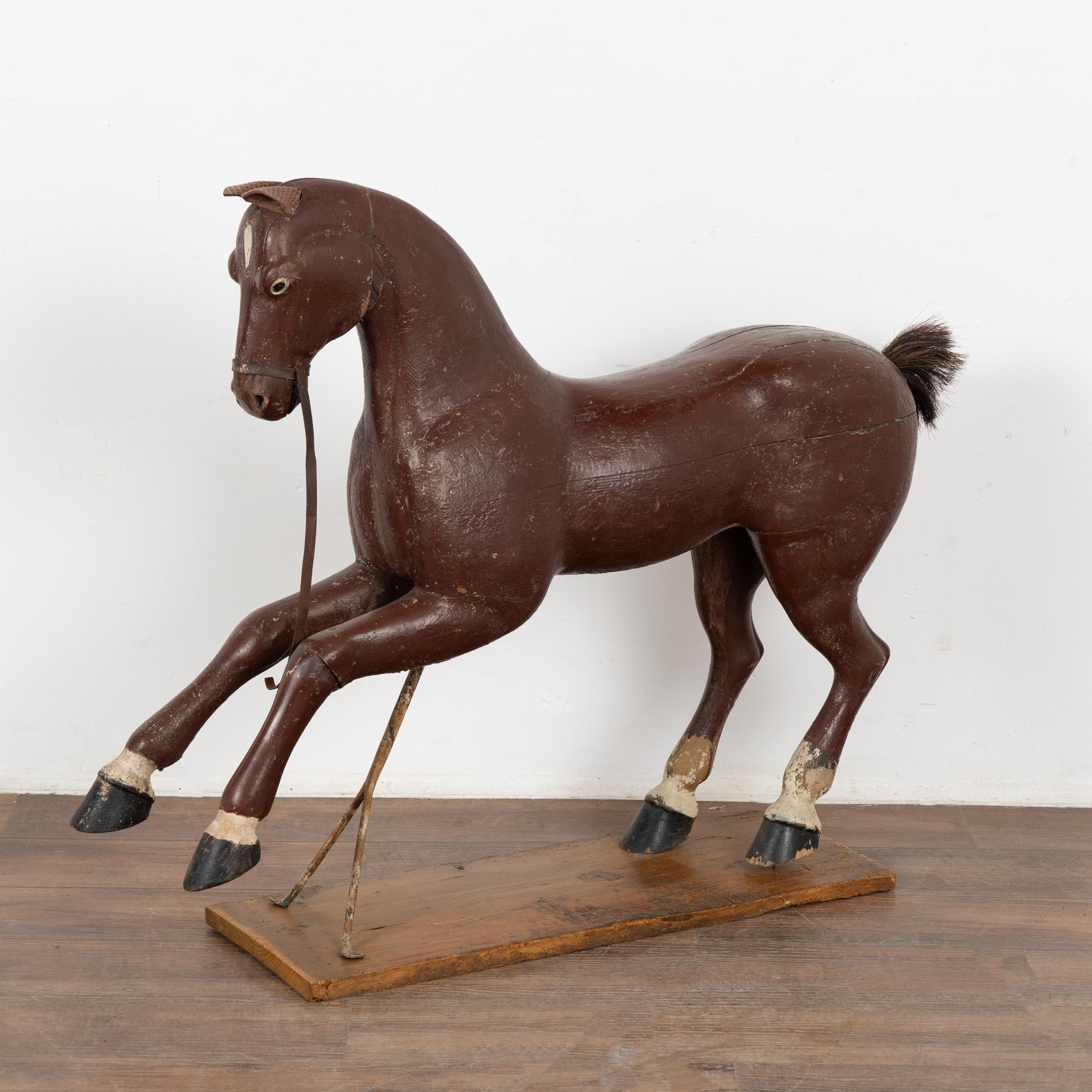 It is the very worn look that creates the wonderful appeal of this original painted and carved horse with metal stand. 
The brown/brick paint has been distressed throughout (and missing under tail). The leather ears, missing mane and broken leather