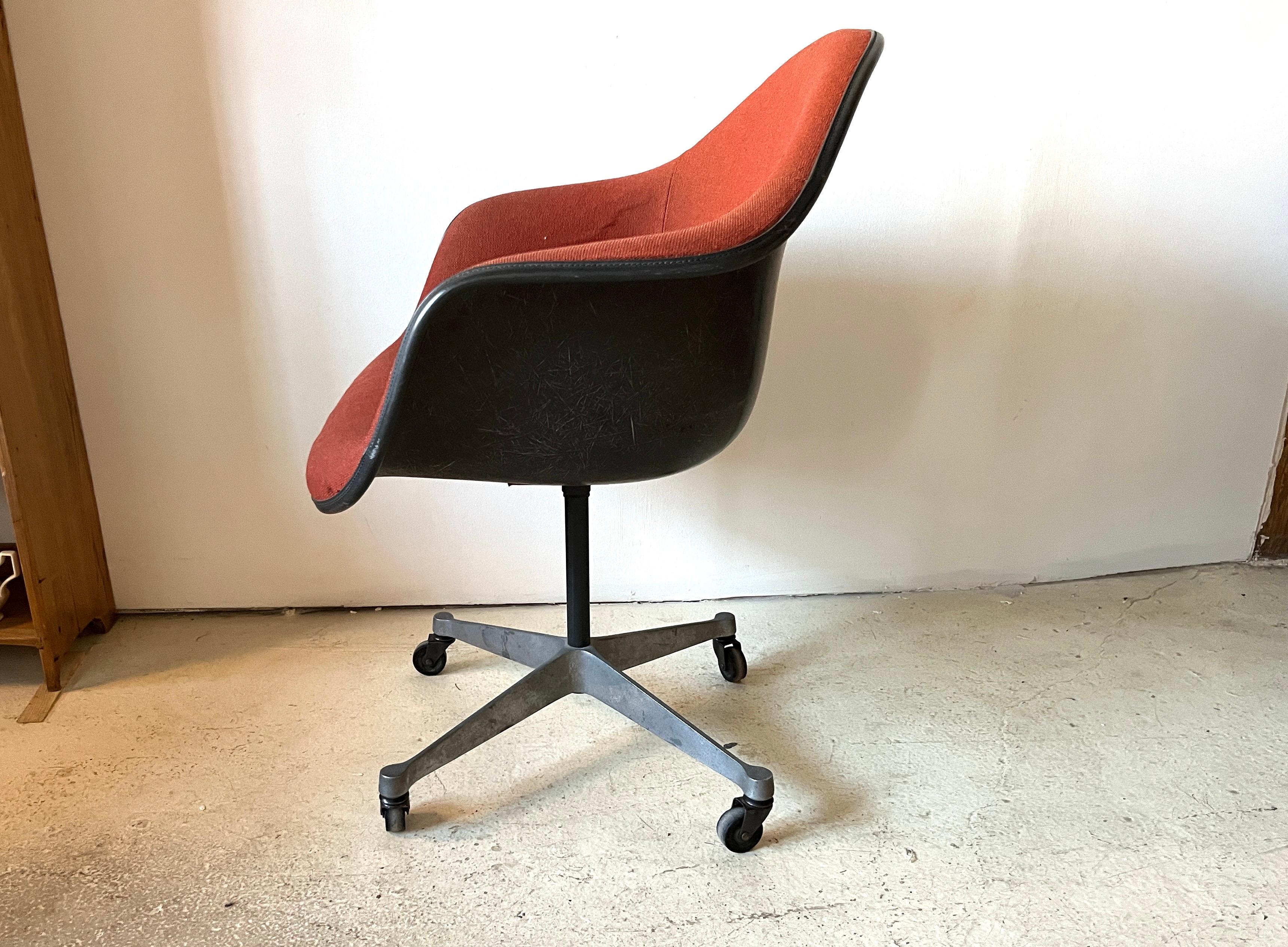 Charles and Ray Eames DAX swivel padded arm shell chair in two-tone with dark gray exposed fiberglass shell. Rusty orange woven wool fabric cover, black piping, four-star aluminium base with casters. Retains remnants of original Herman Miller label.