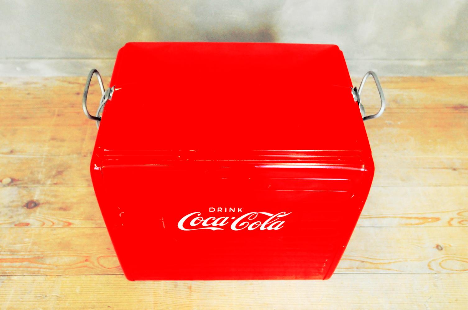 This Coca Cola cooler was bought in the USA in the 1950s or 1960s and brought to Europe. The aluminum box is meant to be filled with ice cubes to keep drinks cool. The top clamps shut.
