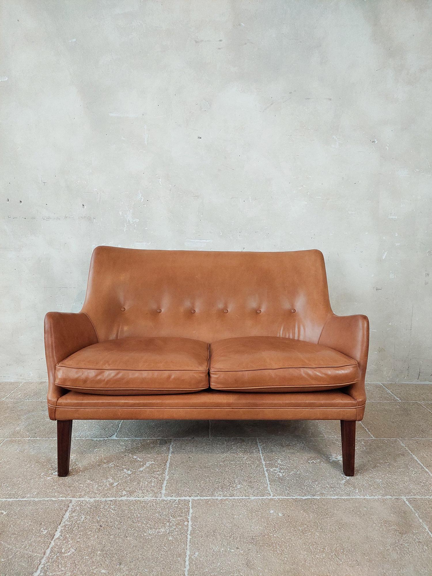 Original two-seat sofa designed by the Danish designer Arne Vodder and manufactured by Ivan Schlechter in 1953. This vintage Scandinavian designer sofa comes in original brown-cognac leather and dark wooden legs and is in very good condition.

h