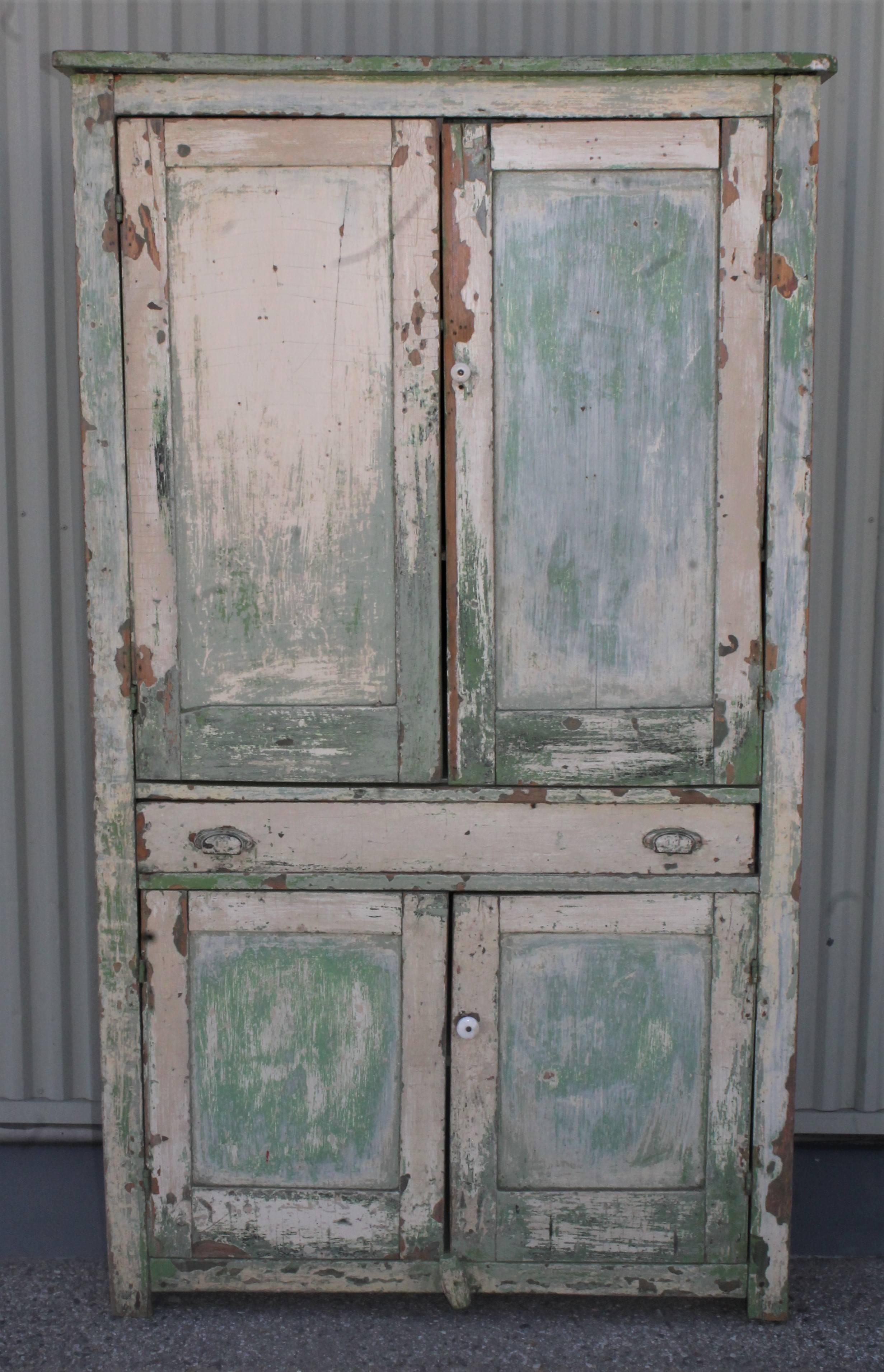 This fine funky Midwestern wall cupboard with a cream over green worn and aged painted surface. This 19th century funky four door wall cupboard is in good, worn condition. The interior is in a original apple green painted surface.