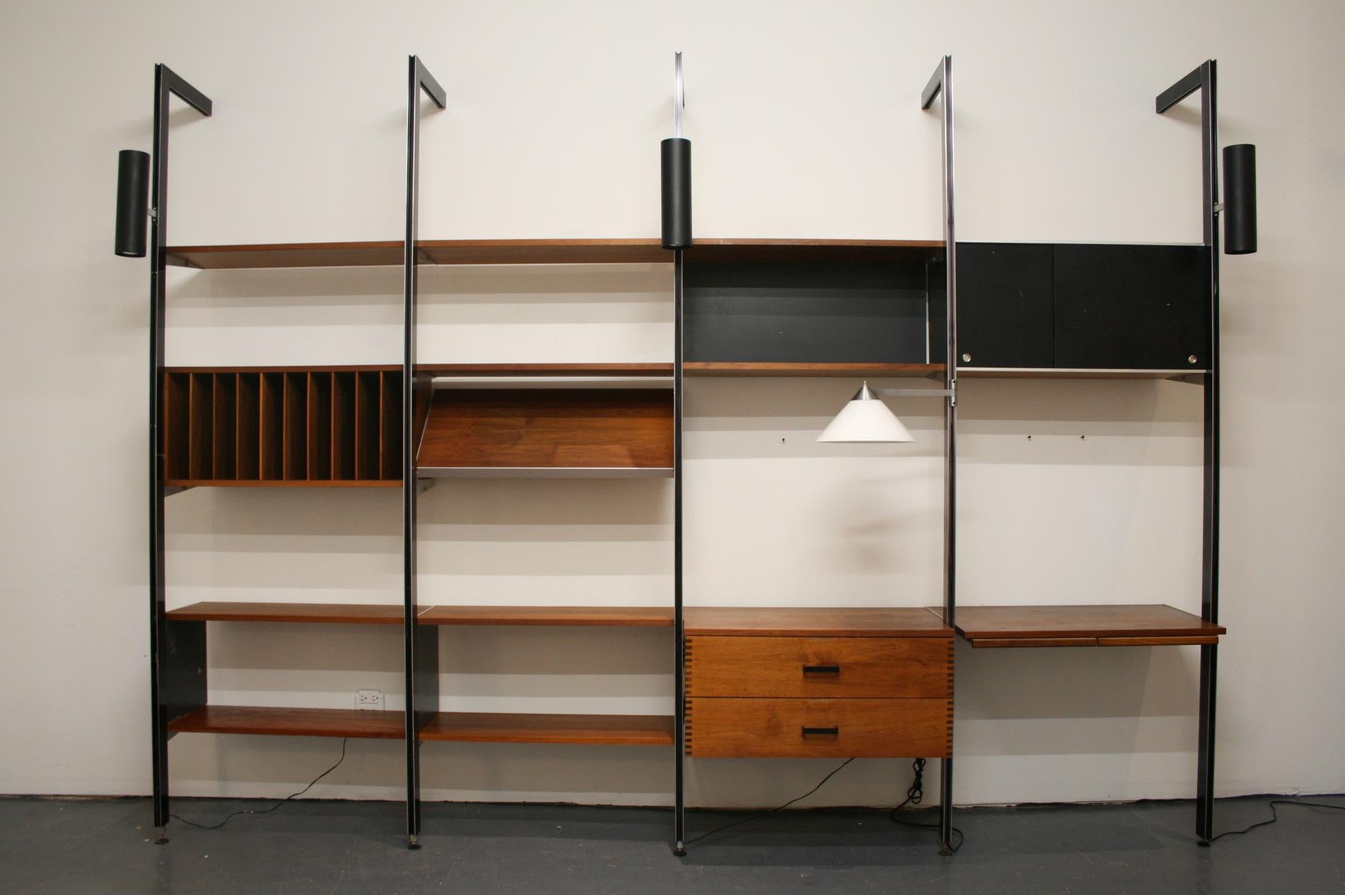 This original design 4 bay wall unit includes:

-5 black anodized aluminum poles with tieback bars for wall installation
-3 black cylinder up/down lights
-1 glass cone desk lamp on swivel arm
-1 -32