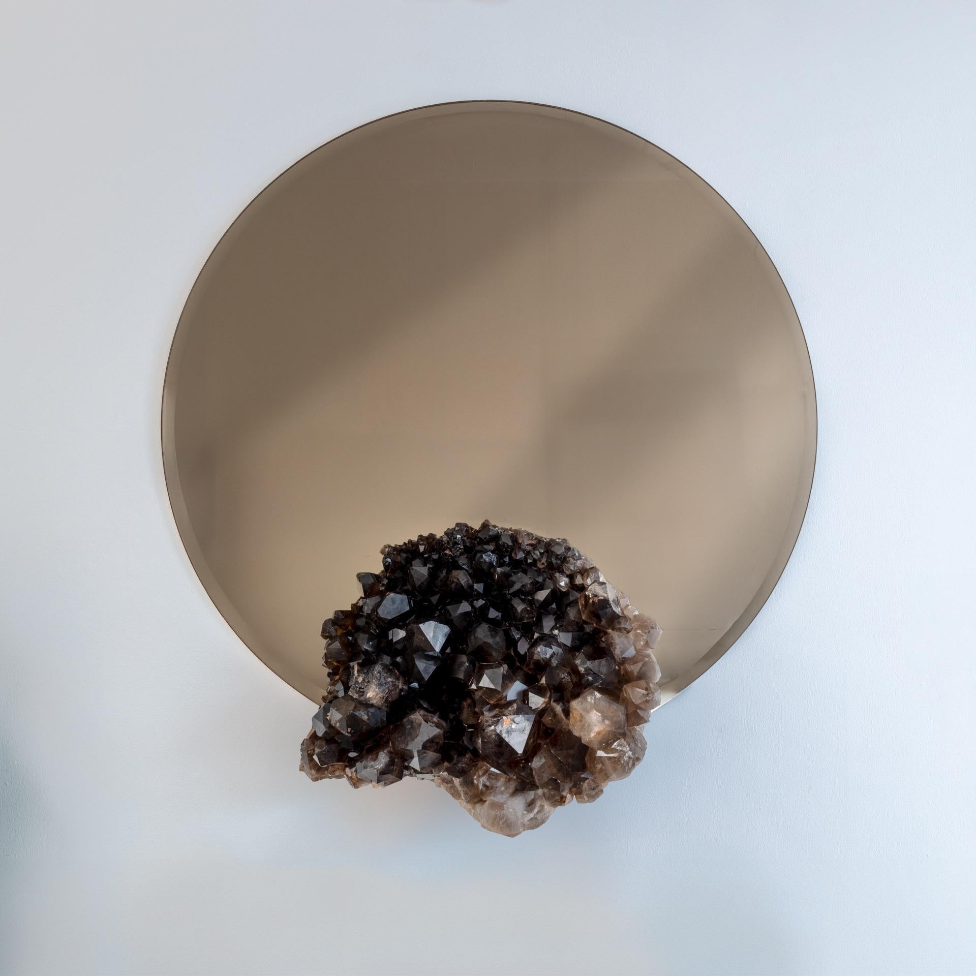 Muro originale  Specchio con cluster di quarzo brasiliano
Questo specchio da parete unico nel suo genere combina un design moderno con la bellezza grezza della natura. Caratterizzato da uno specchio circolare color bronzo, è arricchito da un gruppo