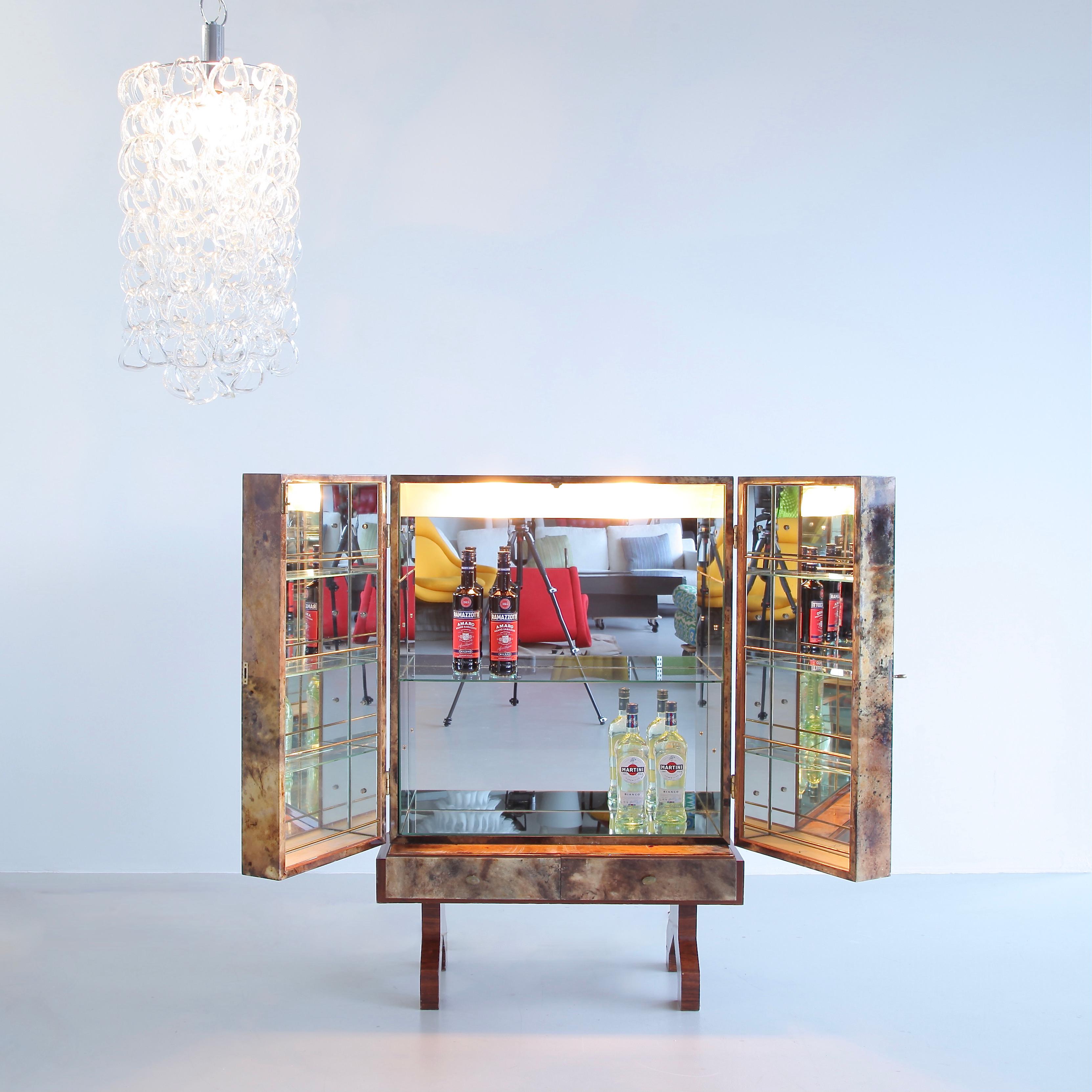 Early dry bar designed by Aldo Tura. Italy, Aldo Tura, 1960s.

Two-door cabinet with two drawers, fully mirrored, glass shelves and inside illumination with door switch. The cabinet is covered in colored and lacquered parchment with brass