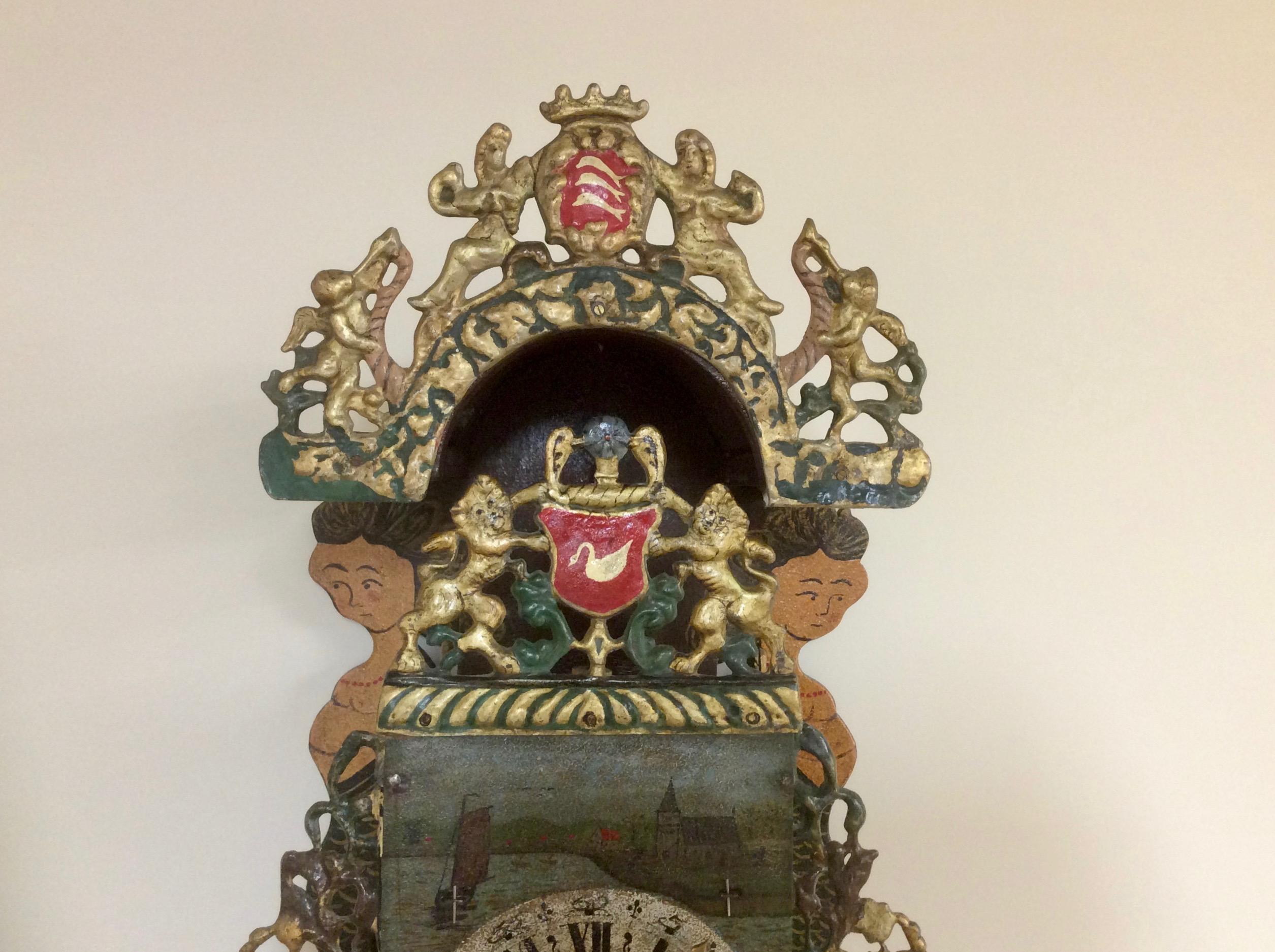 Holländische Stoelklok

Gewölbte Konsole mit zwei gemalten Nixen, vergoldeter Bleikranz mit zwei Löwen neben einem Wappen, seitlich verglaste Fenster mit durchbrochenen Laubsägearbeiten.

Der gemalte Ziffernring mit römischen Ziffern, die