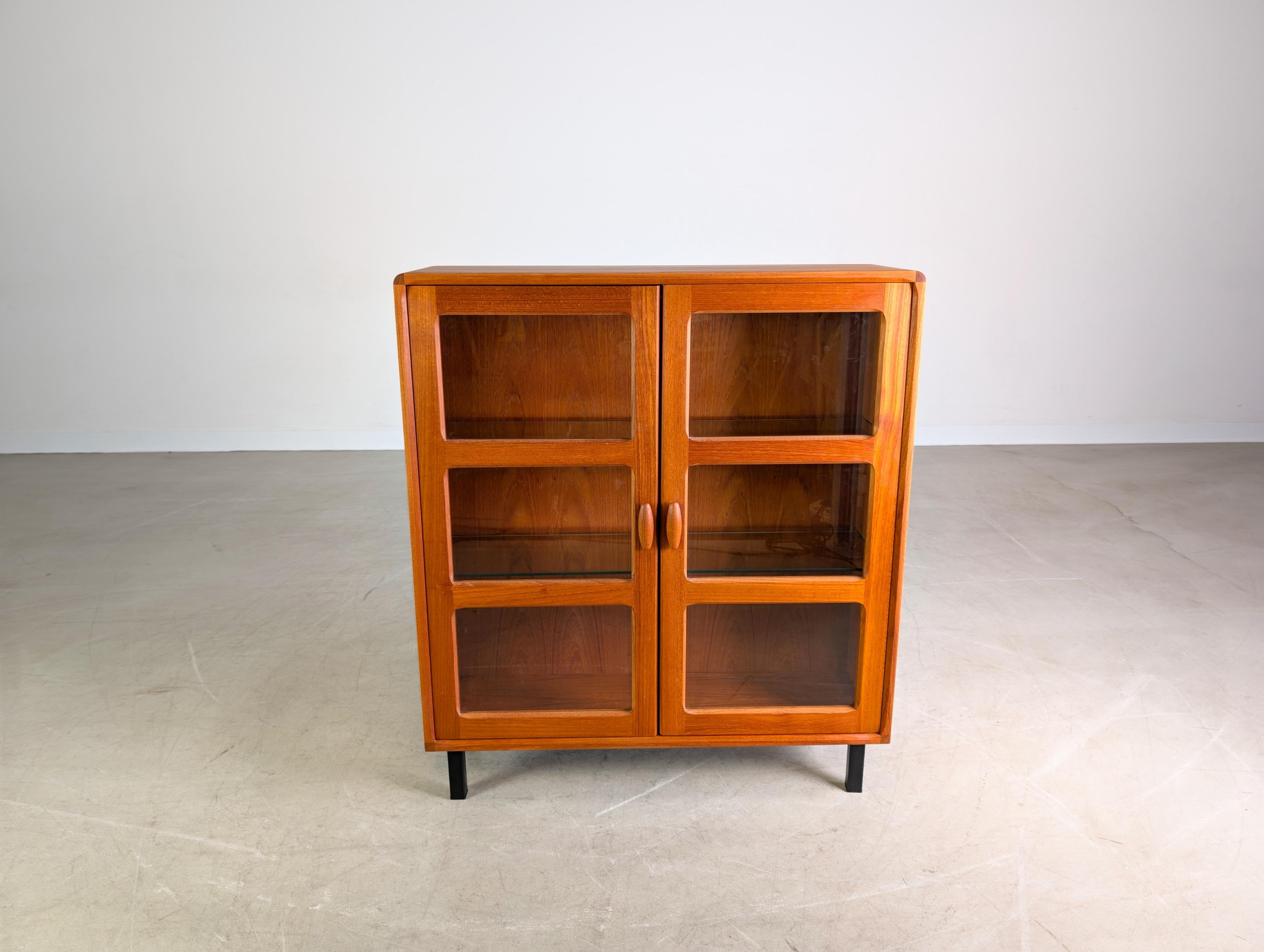 Wir bieten eine wunderschöne kleine Teak Viontage Vitrine von Dyrlund aus den 1960er Jahren zum Verkauf an. Das Holz-Modul wurde professionell aufgearbeitet, mit schlichten Metall-Füßen ausgestattet und lässt sich damit ideal in verschiedenste