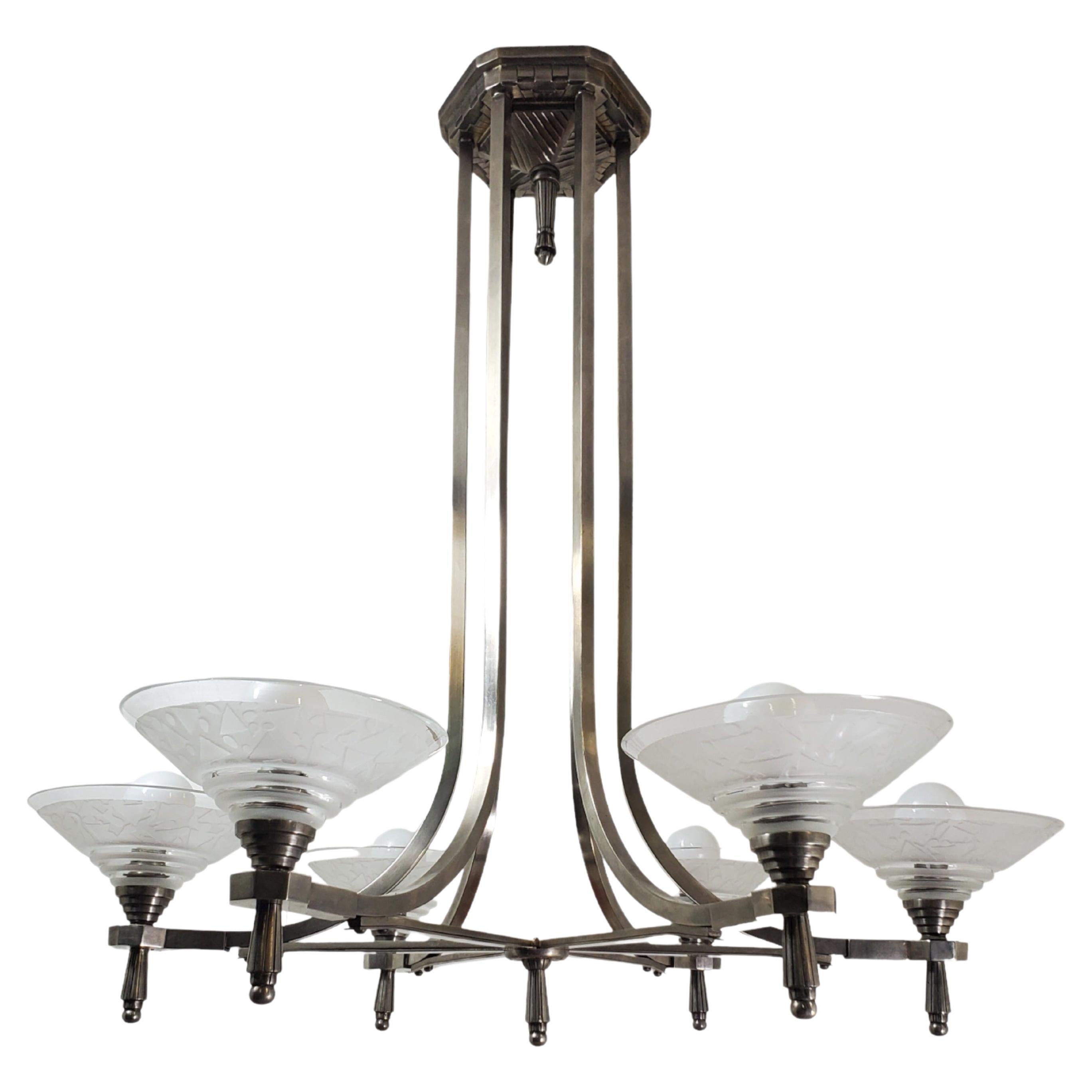 This original and elegant Art Deco chandelier features a nickeled bronzed frame with six branch arms, each gracefully supporting six exquisitely textured acid etched art glass conical cup-shaped shades attributed to Daum Nancy.
The satellite cups