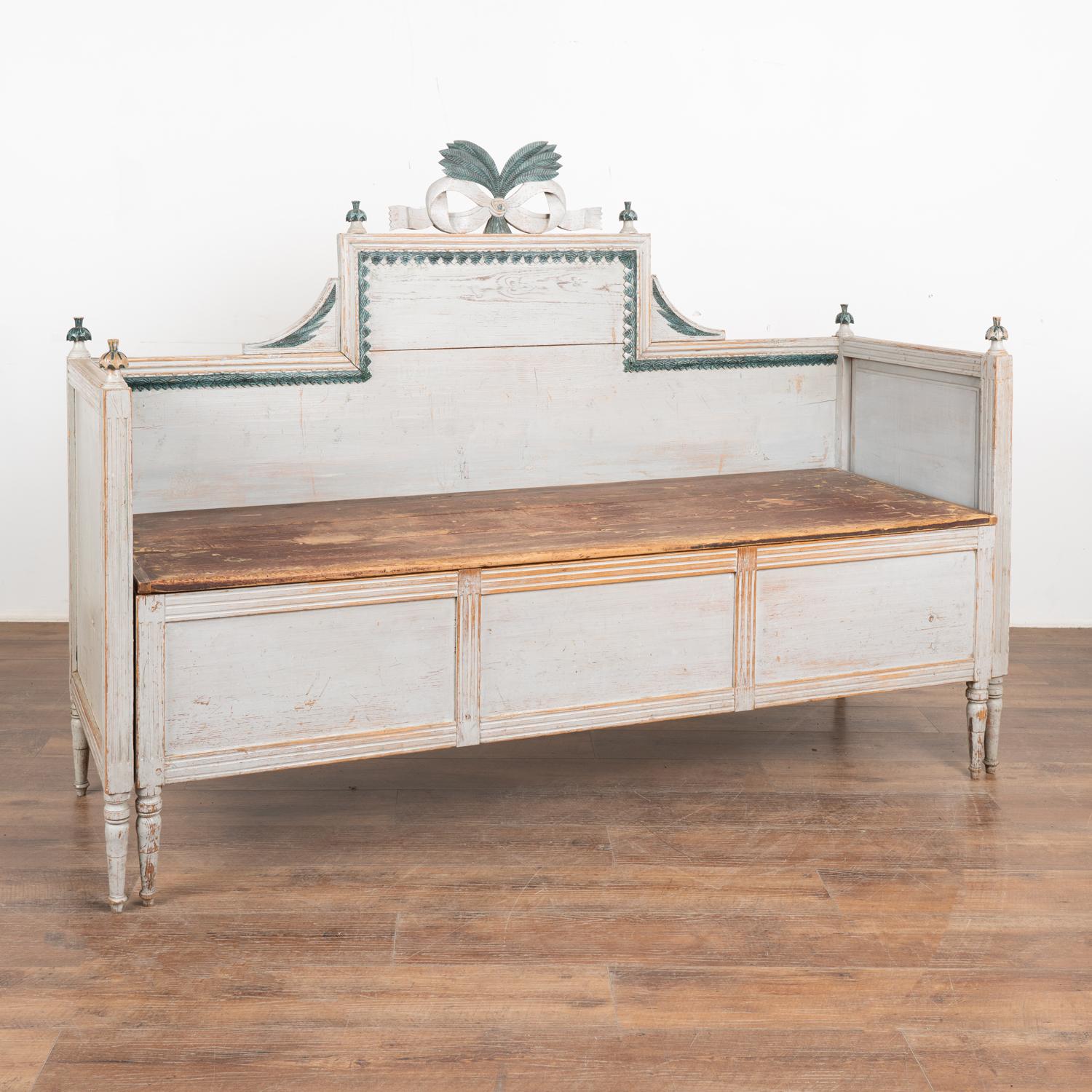 This exceptional Gustavian bench is a special find. Note the original pale gray painted finish (with blue undertones) with decorative finials and carved bow in teal blue/green. The finials, feet, and decorative carved details of the back are all