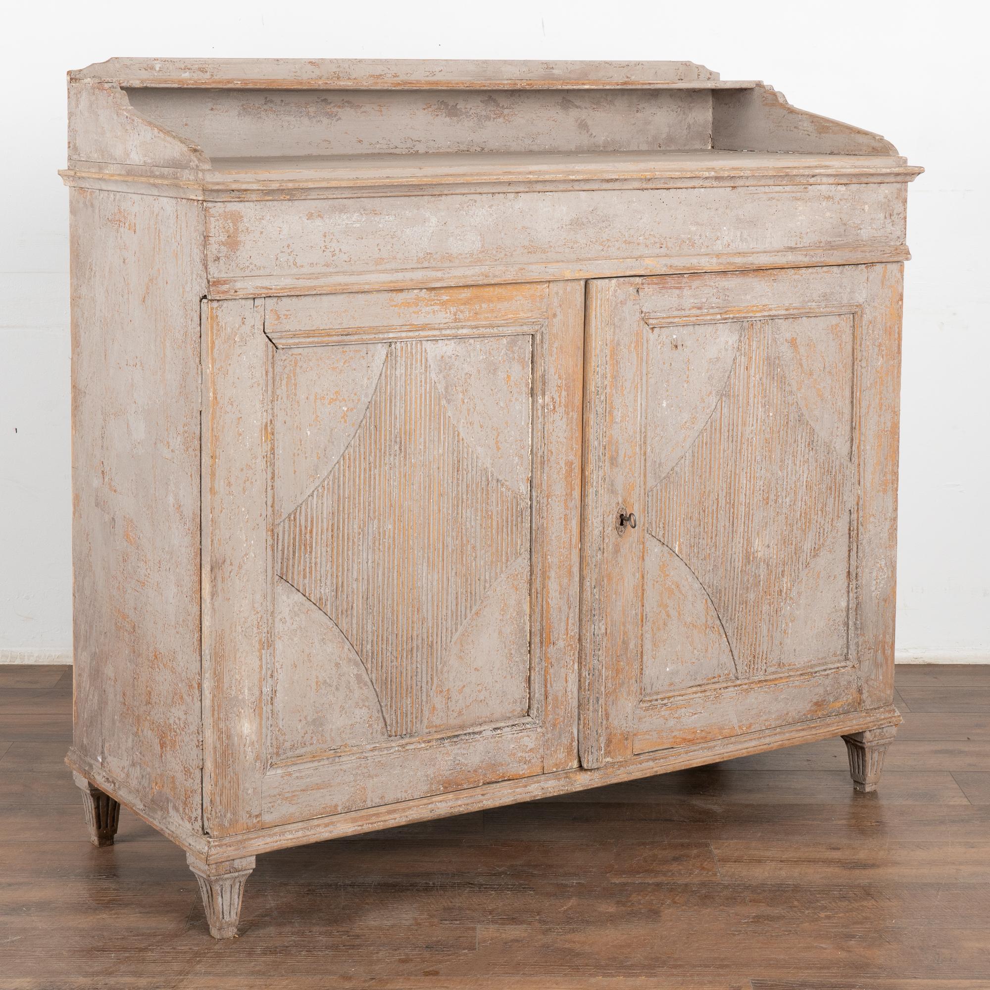 Gustavian gray painted tall pine sideboard or server cabinet with traditional carved fluted diamond panels, tapered fluted feet.
The original gray painted finish has been distressed over years of use, revealing the natural pine wood below while