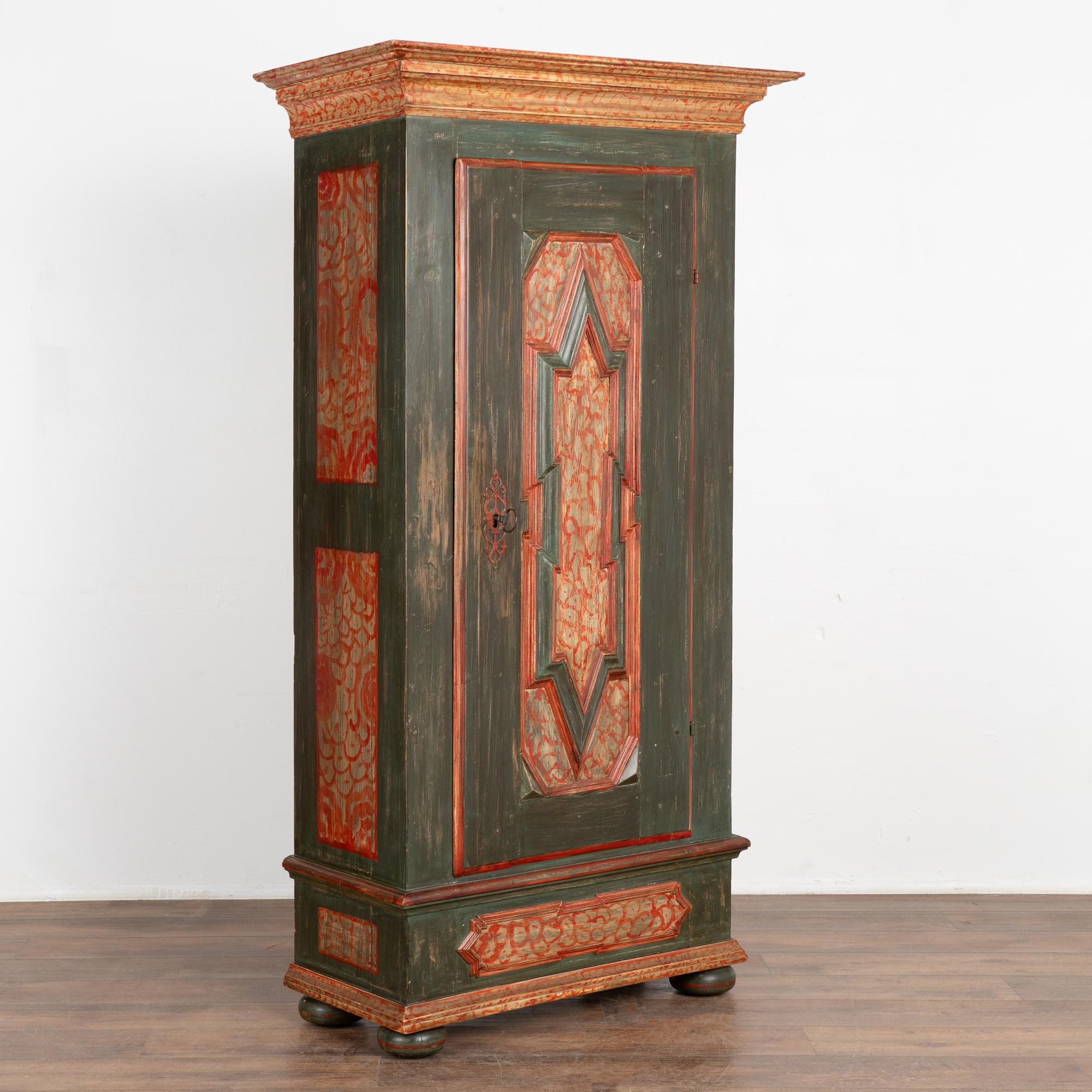 This charming single door armoire is in excellent original condition. The case is painted a dark green with red folk art accents seen in the painted panels, crown and base. 
The original lock mechanism still works, note the interior photo of the