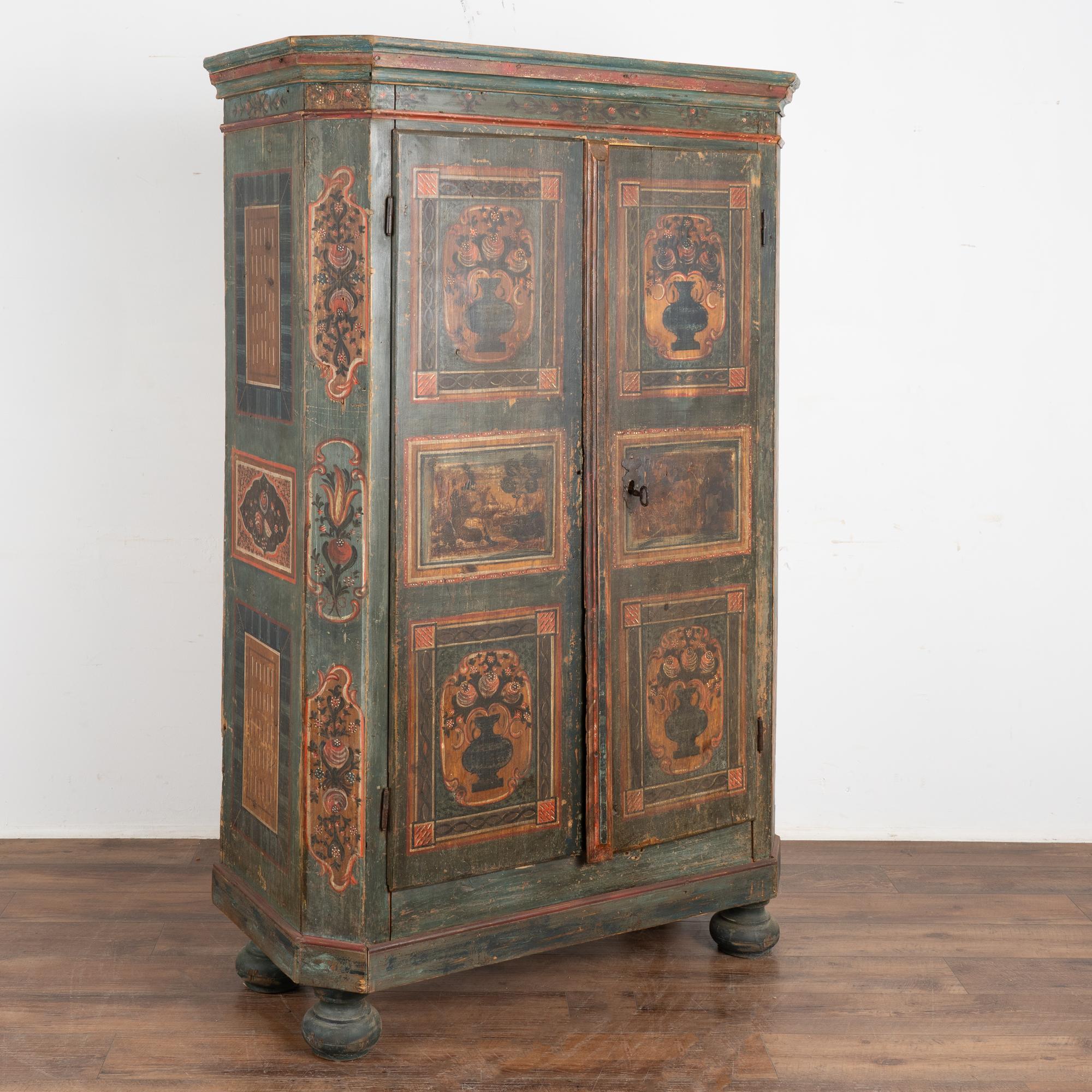 This painted armoire still maintains the quality and details of the original hand-painted finish with background tones of green, teal and blue.
Notice how the 4 panels of flowers in vases on the front doors are accented by additional flowers along