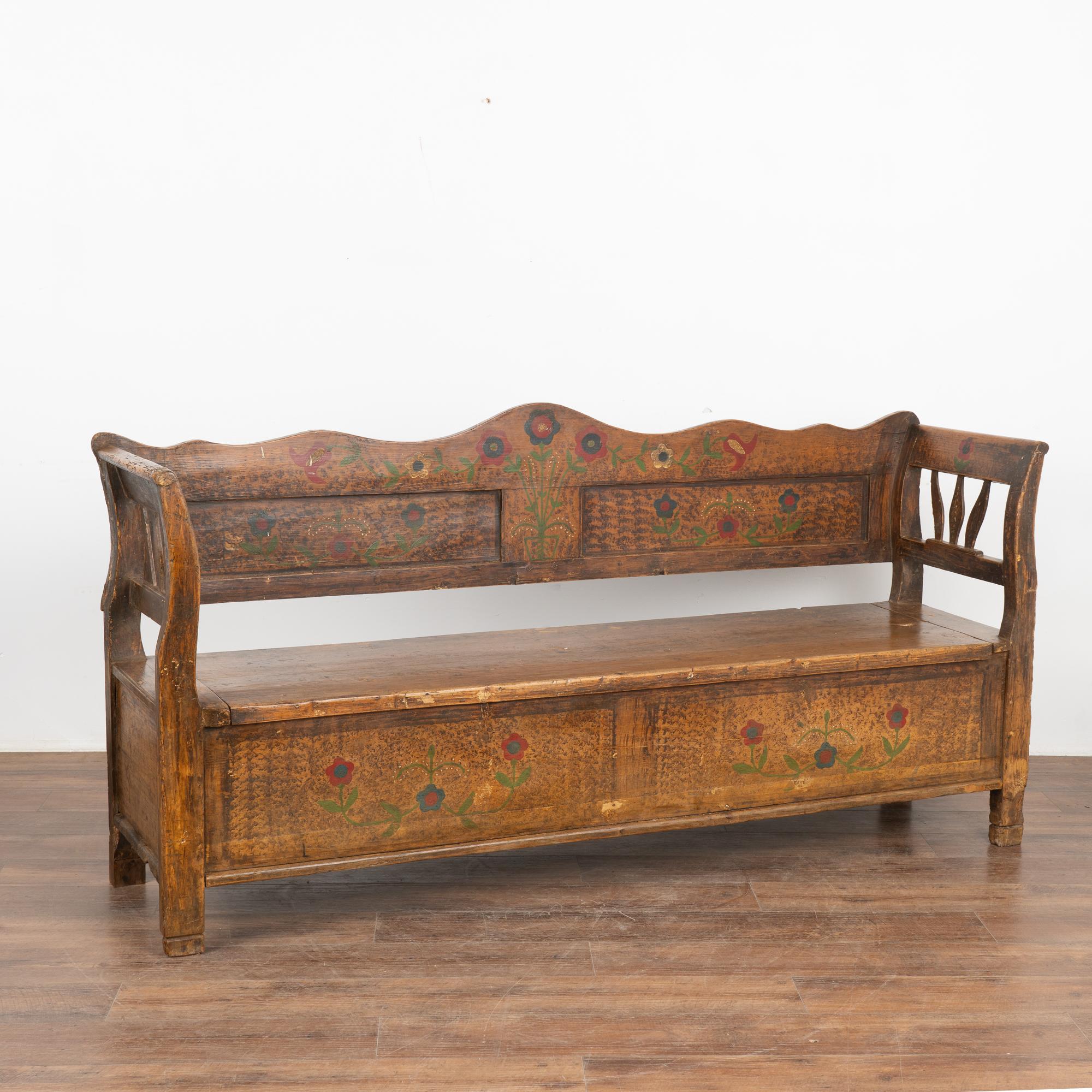 Original hand painted folk art pine bench displays traditional brown faux wood background and colorful red, blue and green floral displays along the front and back.
Hinged bench seat opens to reveal interior divided storage.
Restored, cleaned and