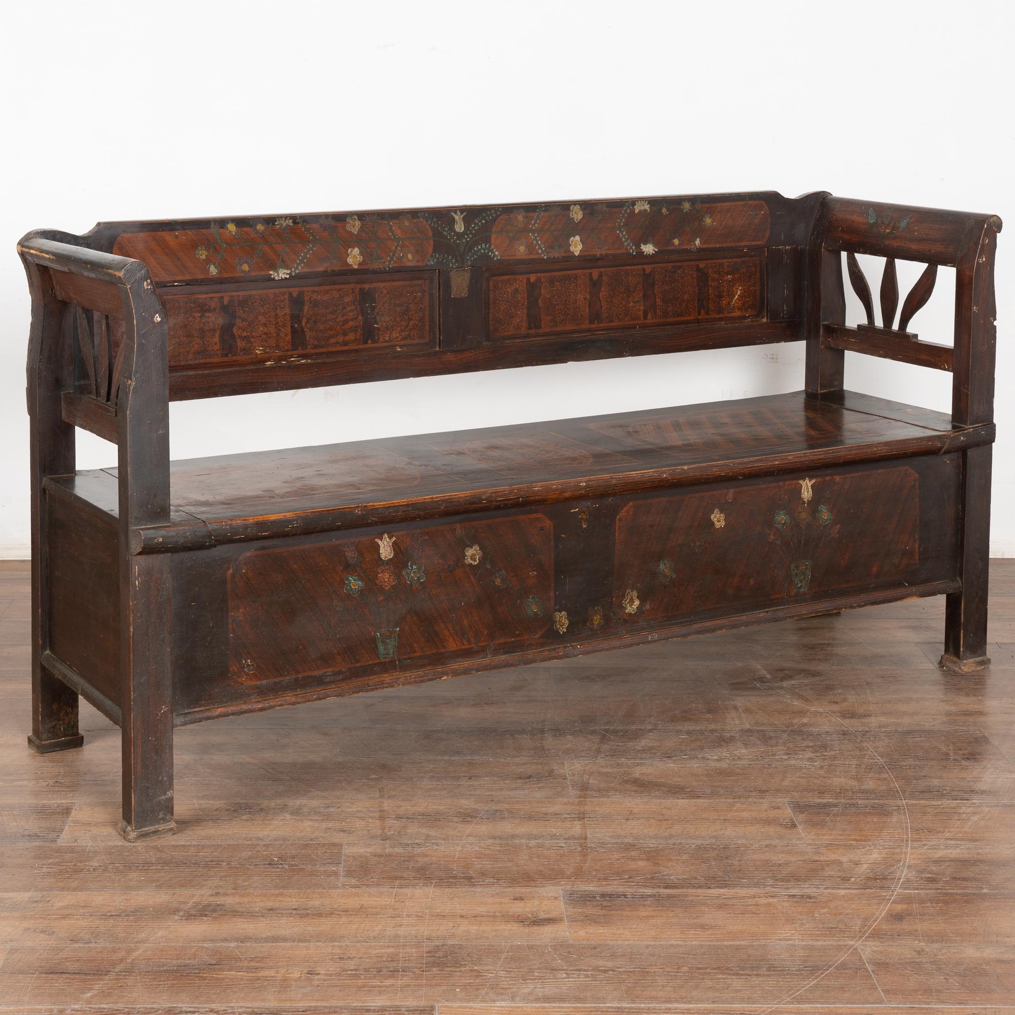 Ce banc en pin, peint à la main, présente un fond traditionnel en faux bois brun et un motif floral.
Dossier solide, accoudoirs légèrement incurvés et banquette rabattable révélant un rangement intérieur (divisé). 
Restauré, nettoyé et ciré, ce banc