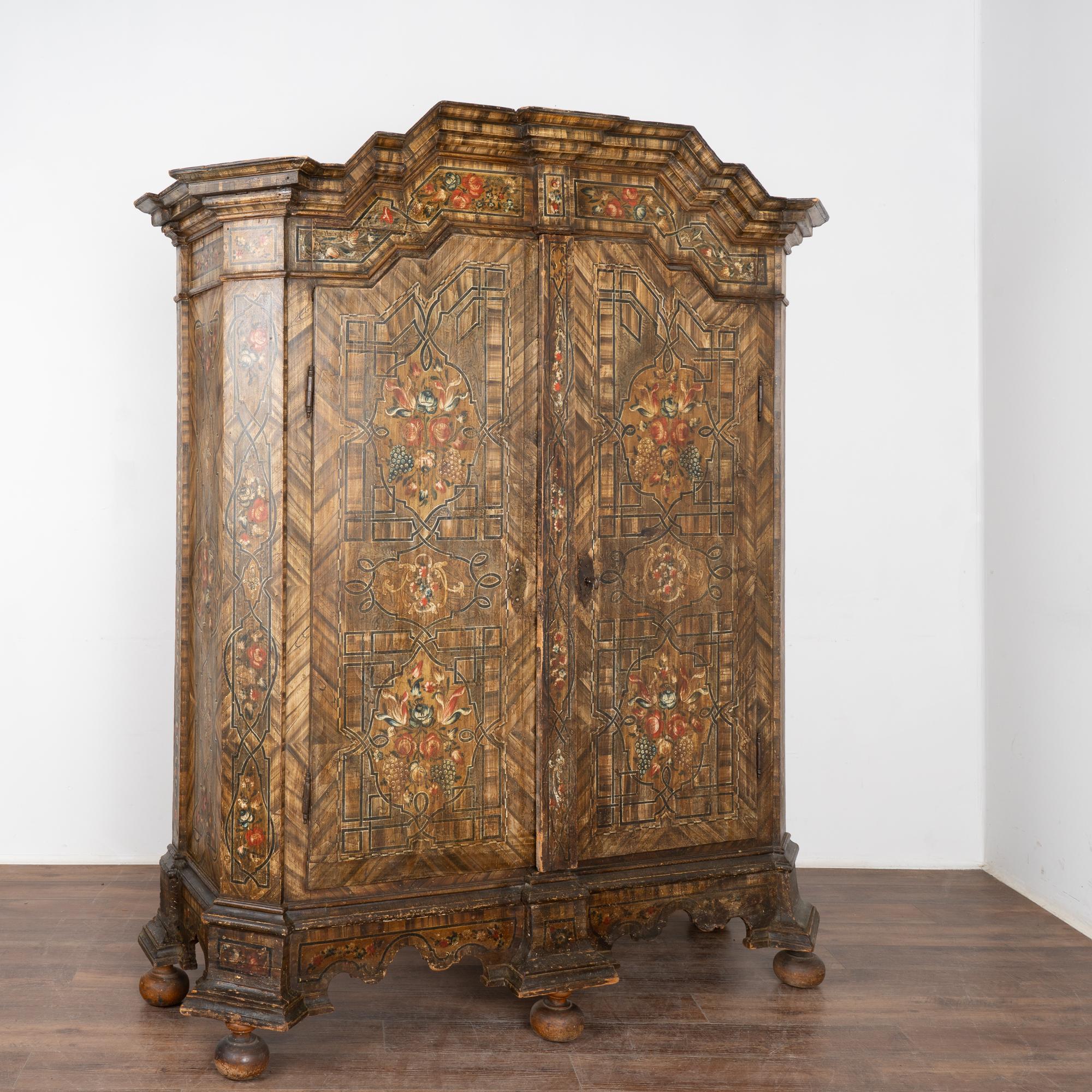 This exceptional armoire still maintains its exquisite original hand-painted details and traditional faux wood background. The earth tones and floral patterns were a typical style element while the geometric border adds a fascinating layer to this