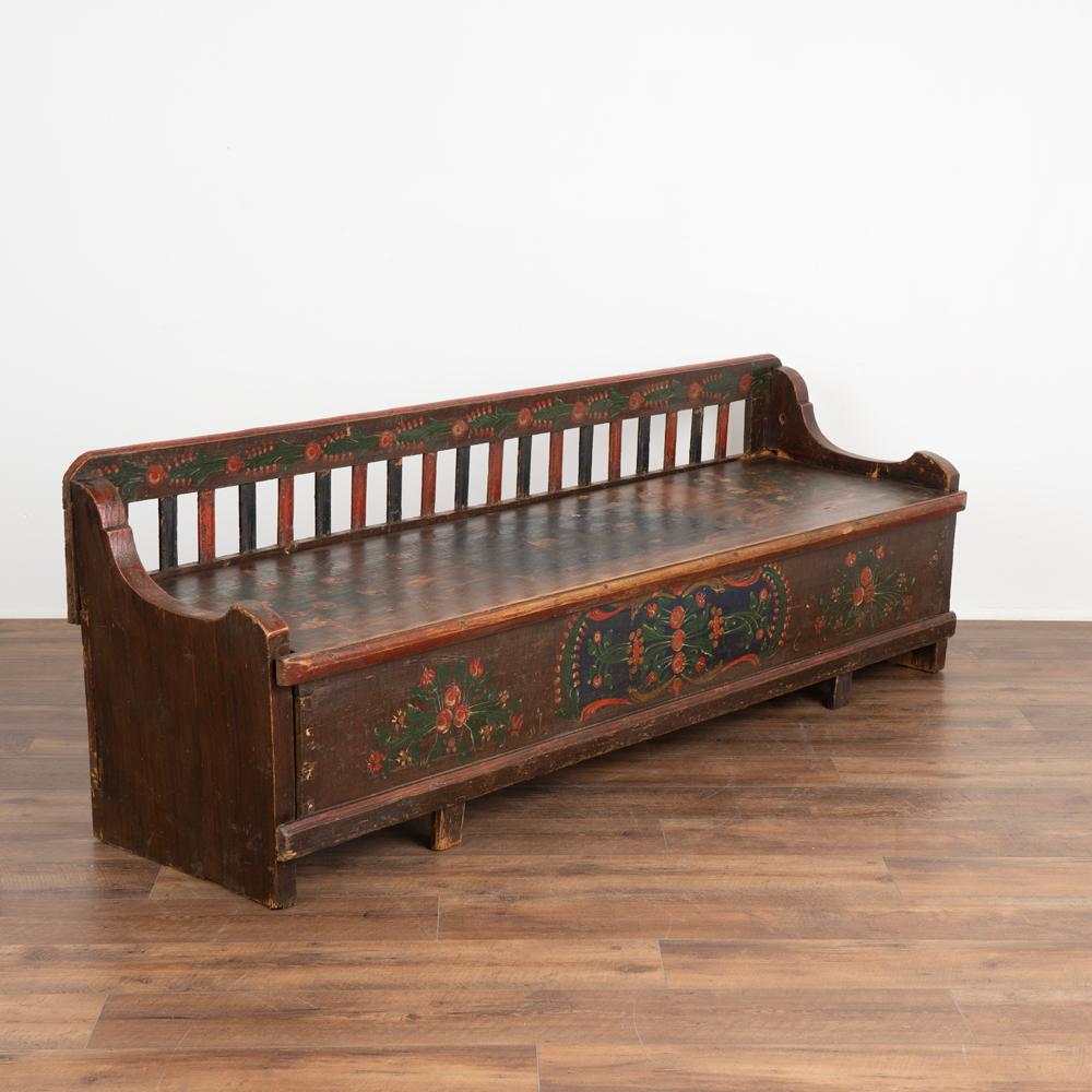 Original hand painted pine bench displays traditional folk art brown faux wood background, blue painted panel with colorful red and green floral motif.
Hinged bench seat reveals interior storage, lower section originally pulled out to allow for