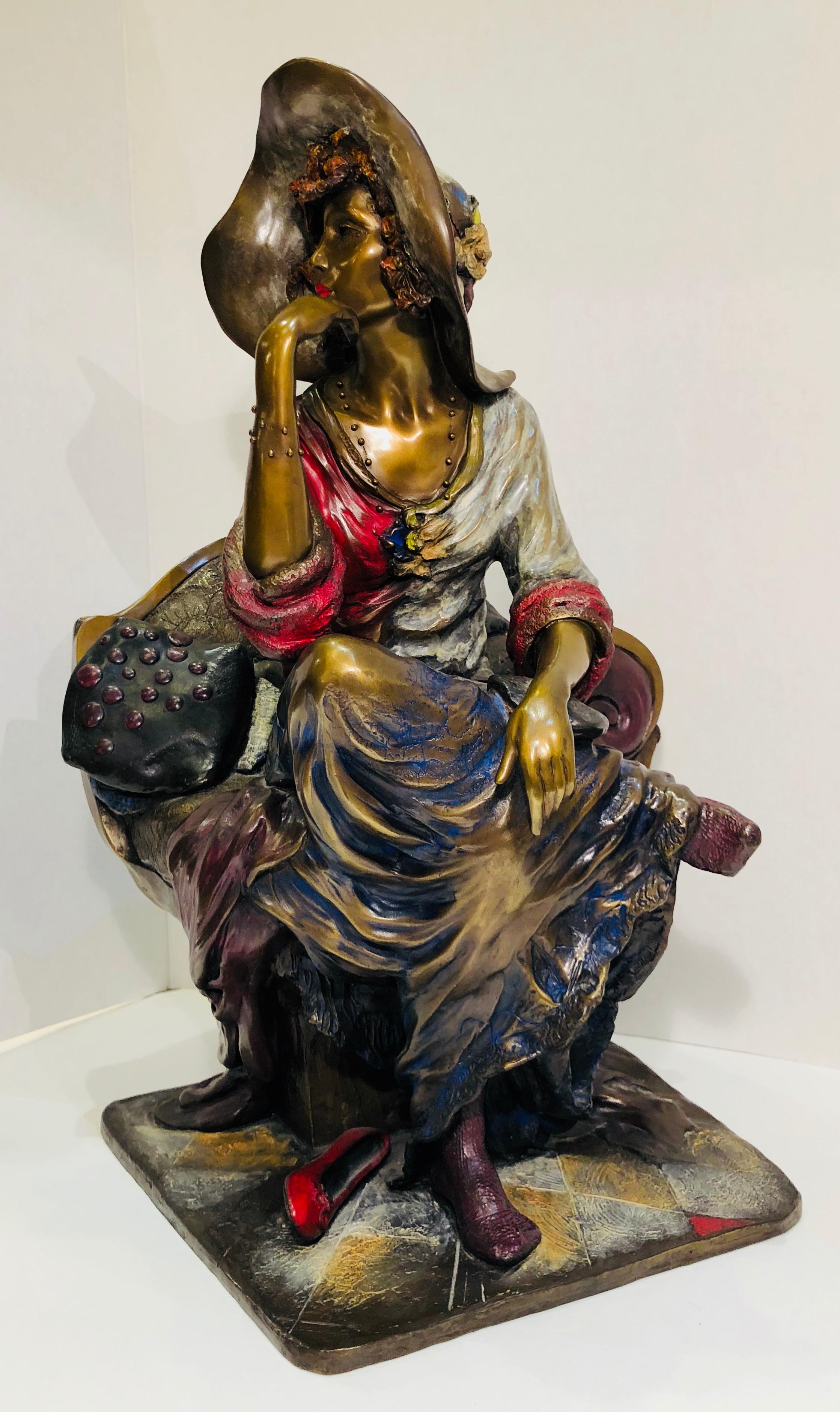 Beautifully detailed, colorful cast bronze sculpture of a seated woman in a large hat and long, flowing skirt, with her shoes kicked off. Her position is alert and thoughtful, yet relaxed, as if she is scanning the crowd for her next dance partner.