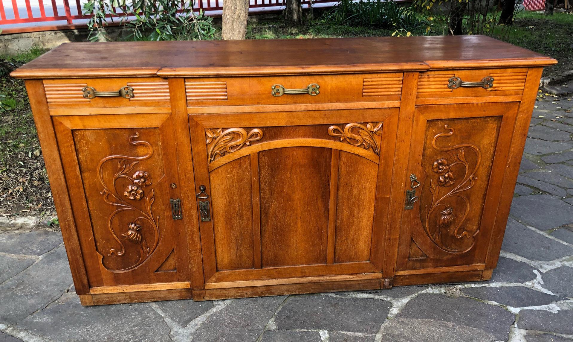 Original Italian art Noveau sideboard in honey-colored,  walnut wood,  with three drawers and three doors, internal shelves.
It is very elegant and of an uncommon shape. 
Each carving was done manually. 
It will be delivered in a specific wooden