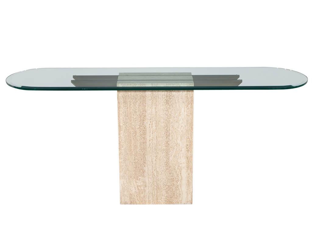 Original Italian Travertine console table with glass top and brass detailing. Featuring beveled edge rounded glass top supported by unique brass pieces within the travertine marble. A sleek narrow piece perfect for hallways or entrances. All