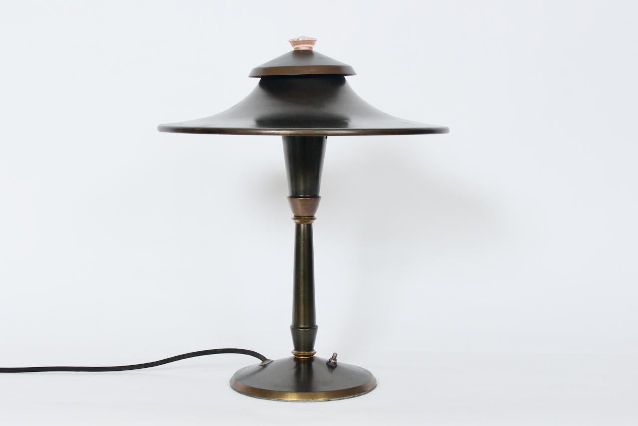 Early Leroy C. Doane for Miller Company, USA brass table lamp. Featuring a Pagoda style with Brass enameled steel surfaces, overall bronzed patina finish, vented double canopy shade, White interior, original Pink glass diffuser finial to top, switch