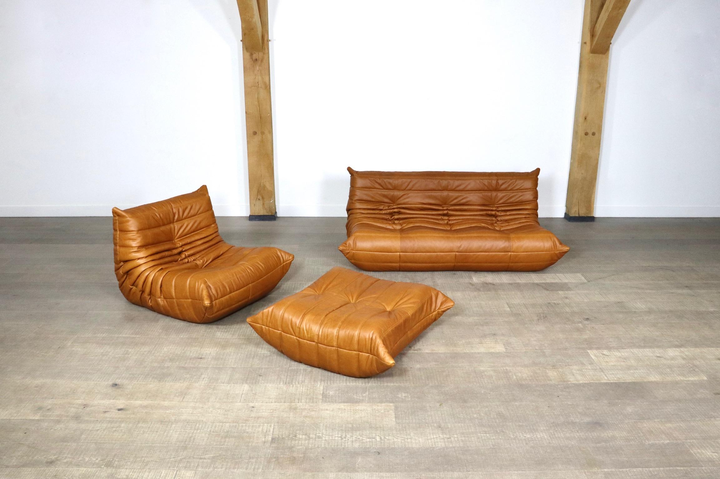 Beautiful cognac leather Togo seating group by Michel Ducaroy for Ligne Roset, 1980s. The entire seating group has the original Ligne Roset logo. The set consists of a 3-seaters, a lounge chair and an ottoman. The beautiful soft leather combines