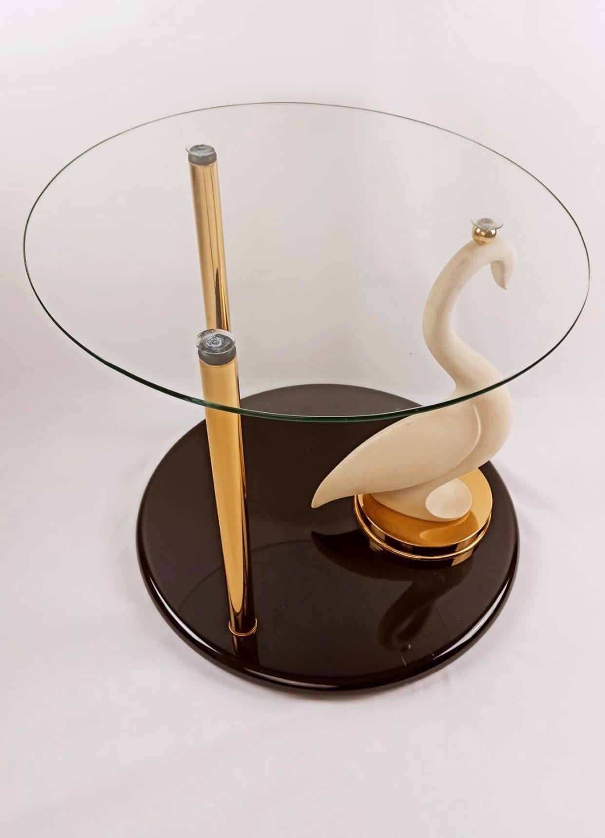This lovely table is composed of a composite swan in ivory colour placed on a lacquered base. The head of the swan and two brass rods hold the glass top. At the base of the swan is signed 