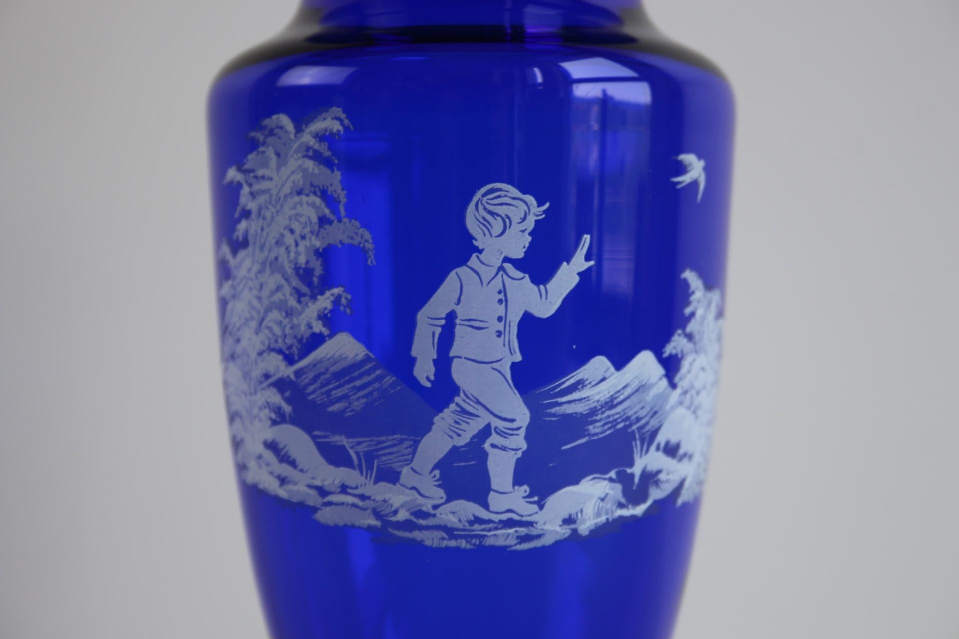 A rare and authentic Mary Gregory glass vase, crafted in deep cobalt blue and featuring her signature white enamel painting. This charming piece from the 