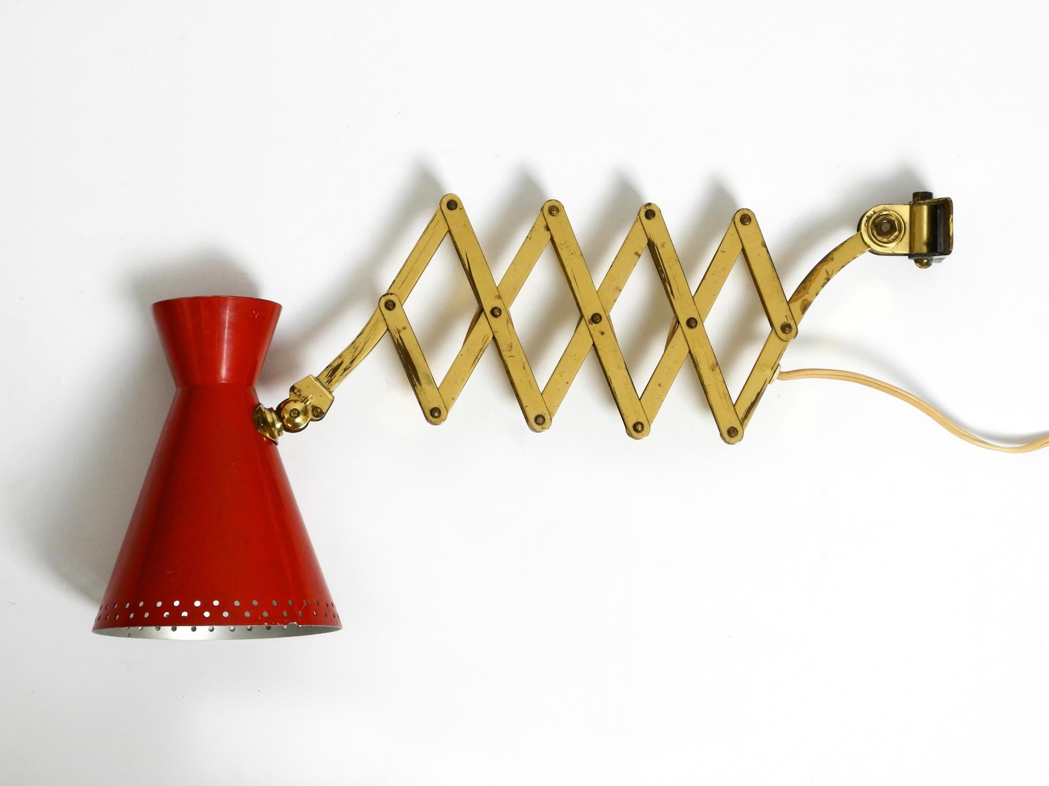 Beautiful original Mid Century brass extendable scissor wall lamp with outside red painted diabolo shade.
Great quality 1950s design. Made in Germany.
The frame is made entirely of brass, the shade is made of aluminium.
The shade can be rotated