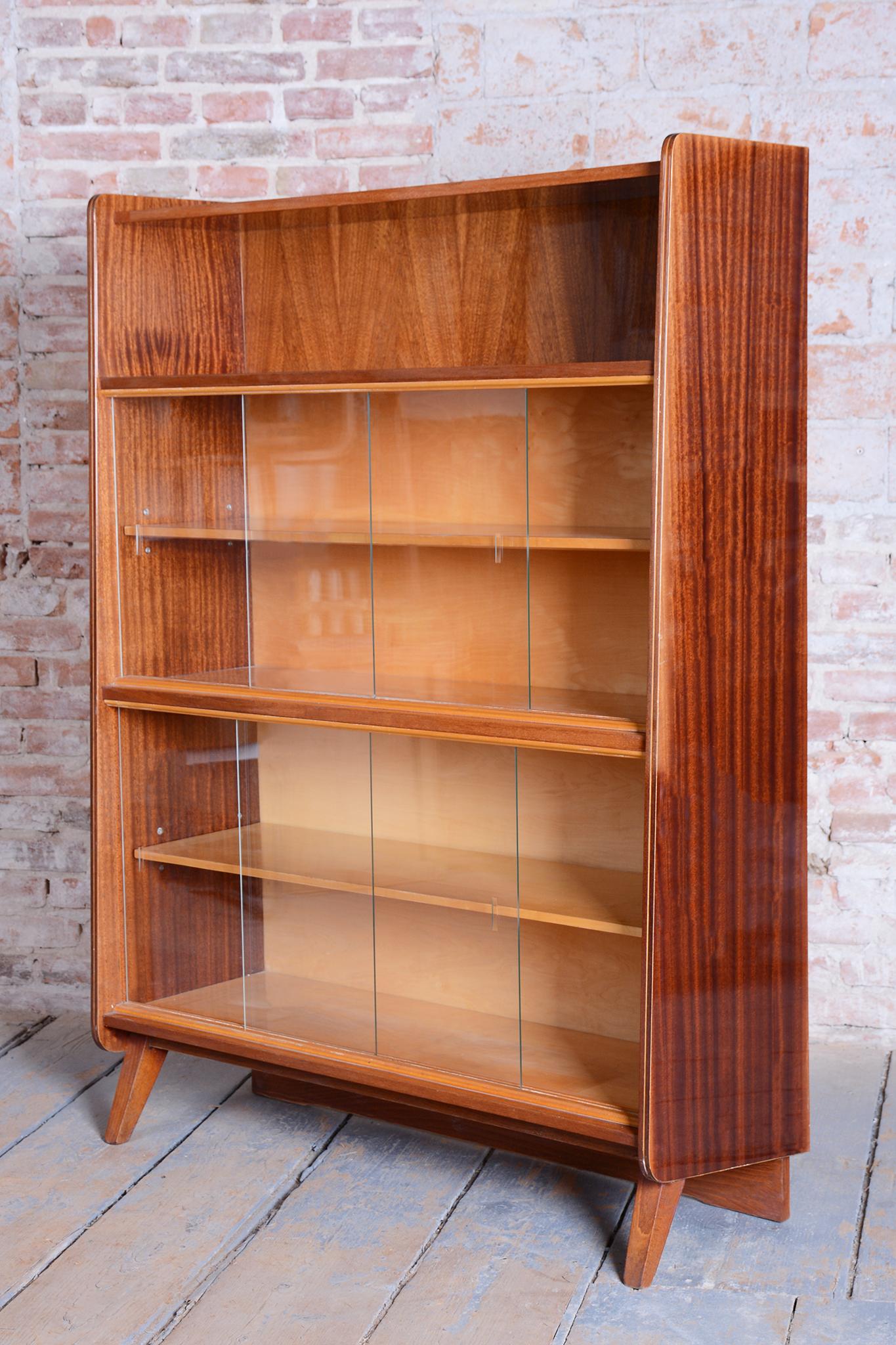This elegant Mid-Century display cabinet comes from Czechoslovakia from the mid-20th century. It is made of mahogany wood and boasts a high-gloss finish. The cabinet was manufactured by the national enterprise Nový domov, n.p., Spišská Nová Ves,