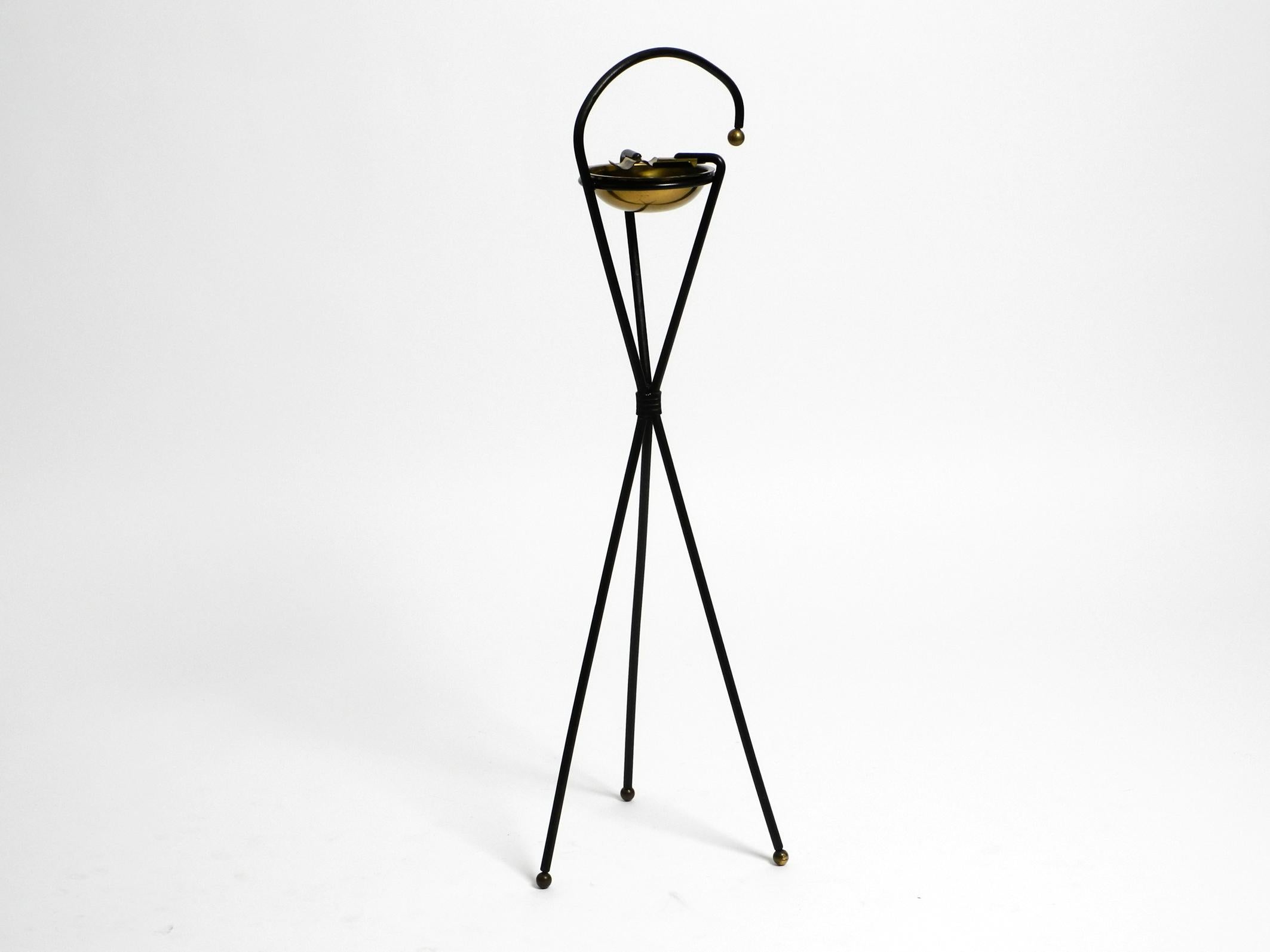 Super chic original Mid Century tripod standing ashtray with a gorgeous patina.
Solid iron frame painted in black.
The bowl, the cigarette holders and the balls on the base and on the handle are made of brass.
Beautiful minimalist design from the