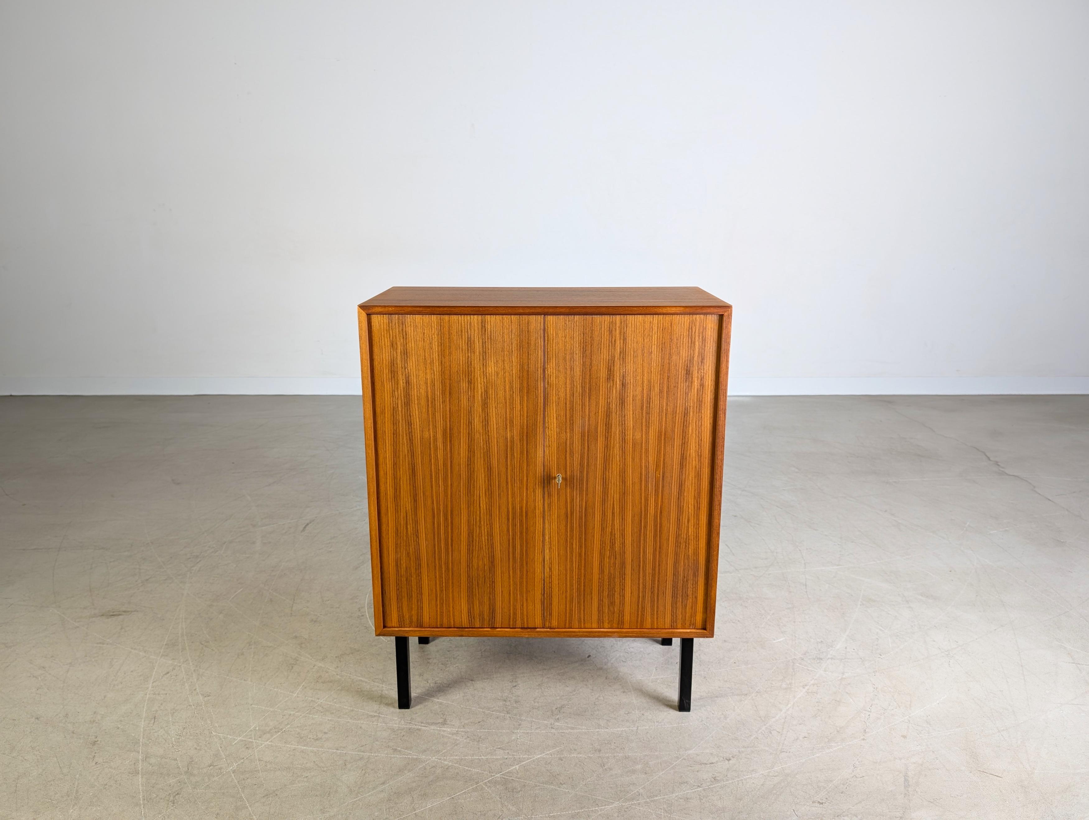 Wir bieten eine hochwertige kleine Kommode aus Nussbaumholz aus den 1960er Jahren zum Verkauf an. Das Möbel verfügt über zwei abschließbare Türen und lässt sich aufgrund seiner minimalistischen Formgebung sehr gut auch in moderne Wohnräume