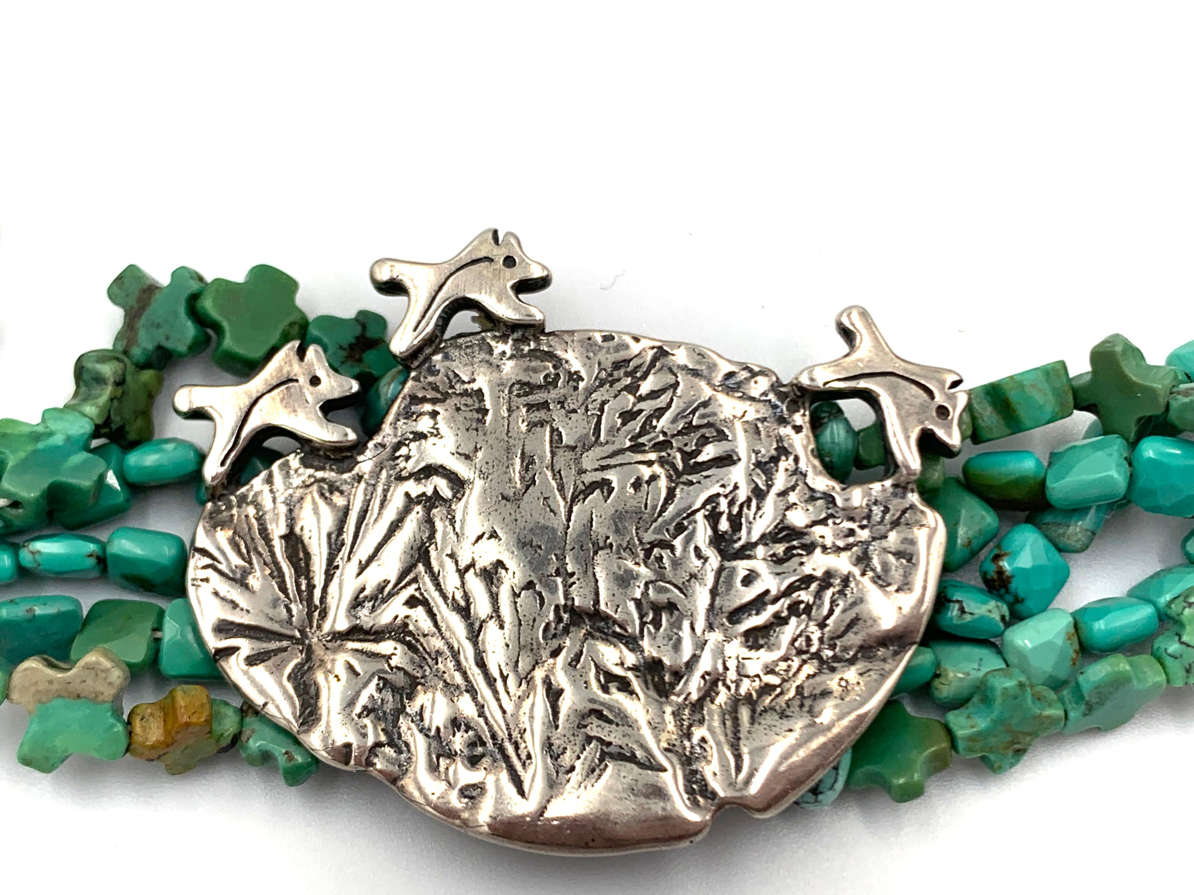 Turquoise coyotes, three silver coyotes race over a silver coin bordered by turquoise cubes and Hopi morning stars. 

Mary and Doug Hancock, of Mummy’s Bundle, create beautiful wearable art jewelry inspired by the ancient Indian cultures. Doug an