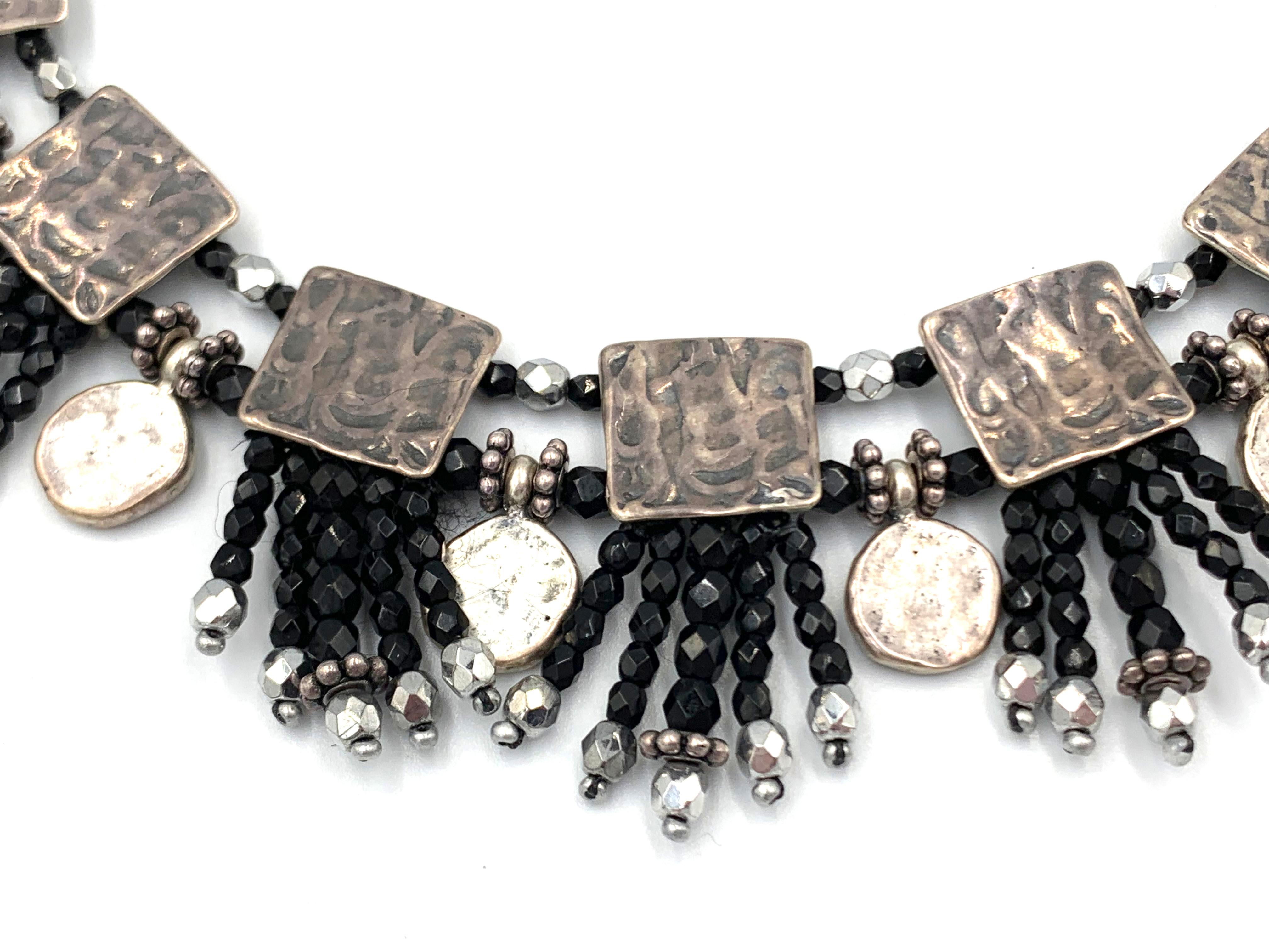 Il collare d'argento e nero, i pendenti quadrati d'argento e la ciambella a forma di palla proveniente dall'India sono separati da perle di vetro ceco nero. - descrizione originale scritta a mano da Mary Hancocks

Mary e Doug Hancocks, di Mummy's