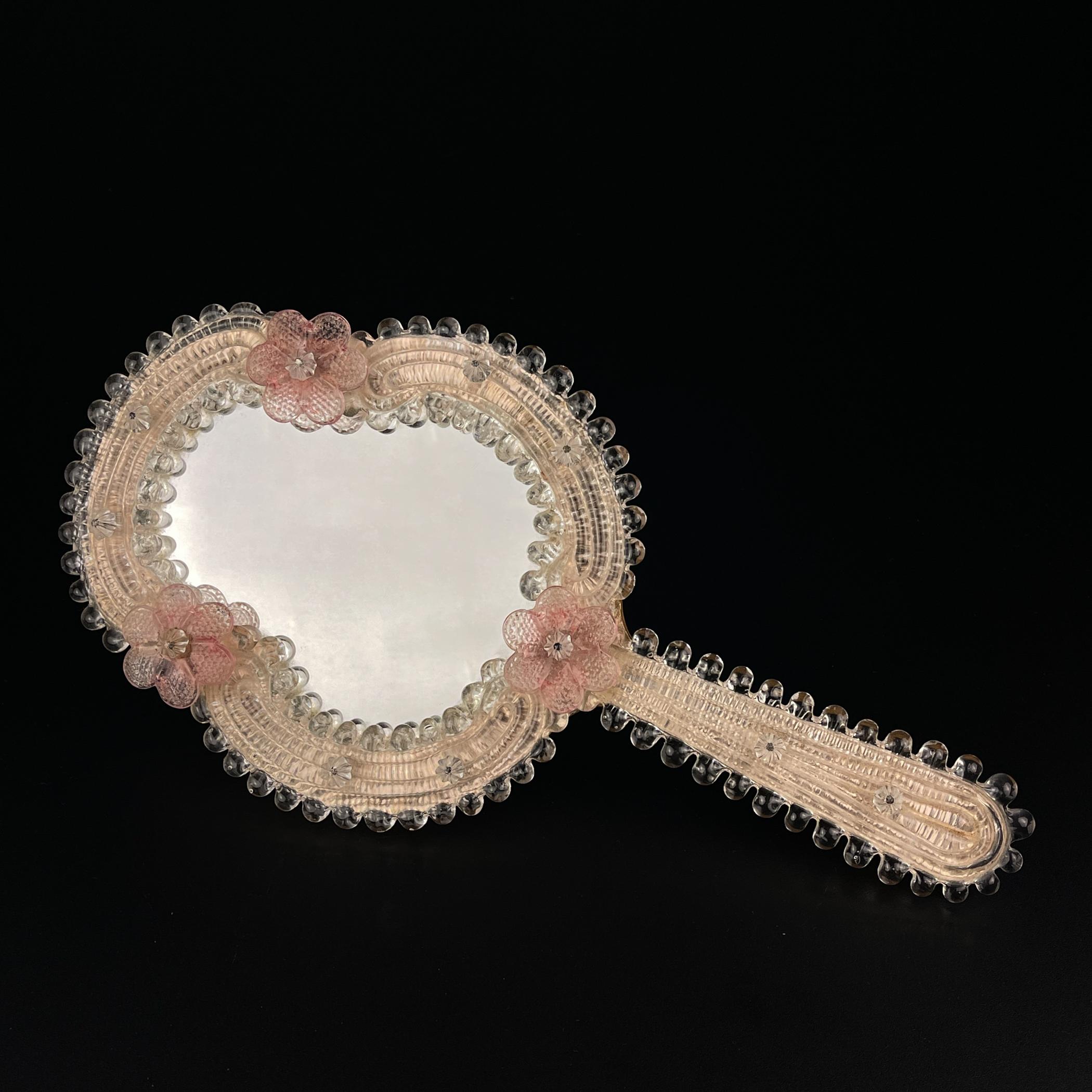 Charmanter Spiegel aus Murano-Glas, hergestellt in Venedig (Italien) in den 1950er Jahren. Der Spiegel kann als Handspiegel oder Wandspiegel verwendet werden.
Der Spiegel ist in einem guten, alten Zustand.

Abmessungen:
Breite: 17 cm / 6,7