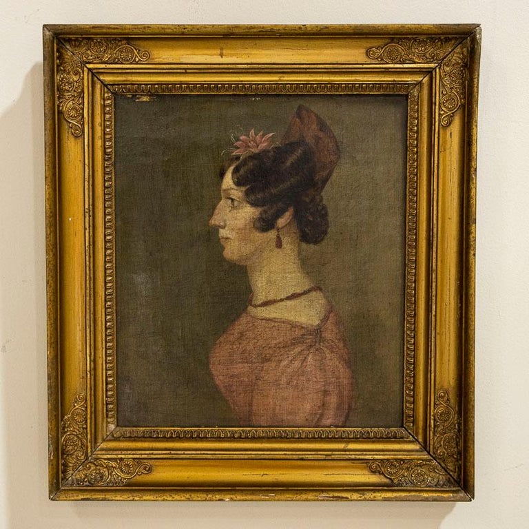 A delightful original oil on canvas portrait of a lady in profile wearing a pink dress, coral jewelry and a flower embellishment in her hair. Painter unknown, first half of 19th century. Condition includes craquelure throughout and few minor